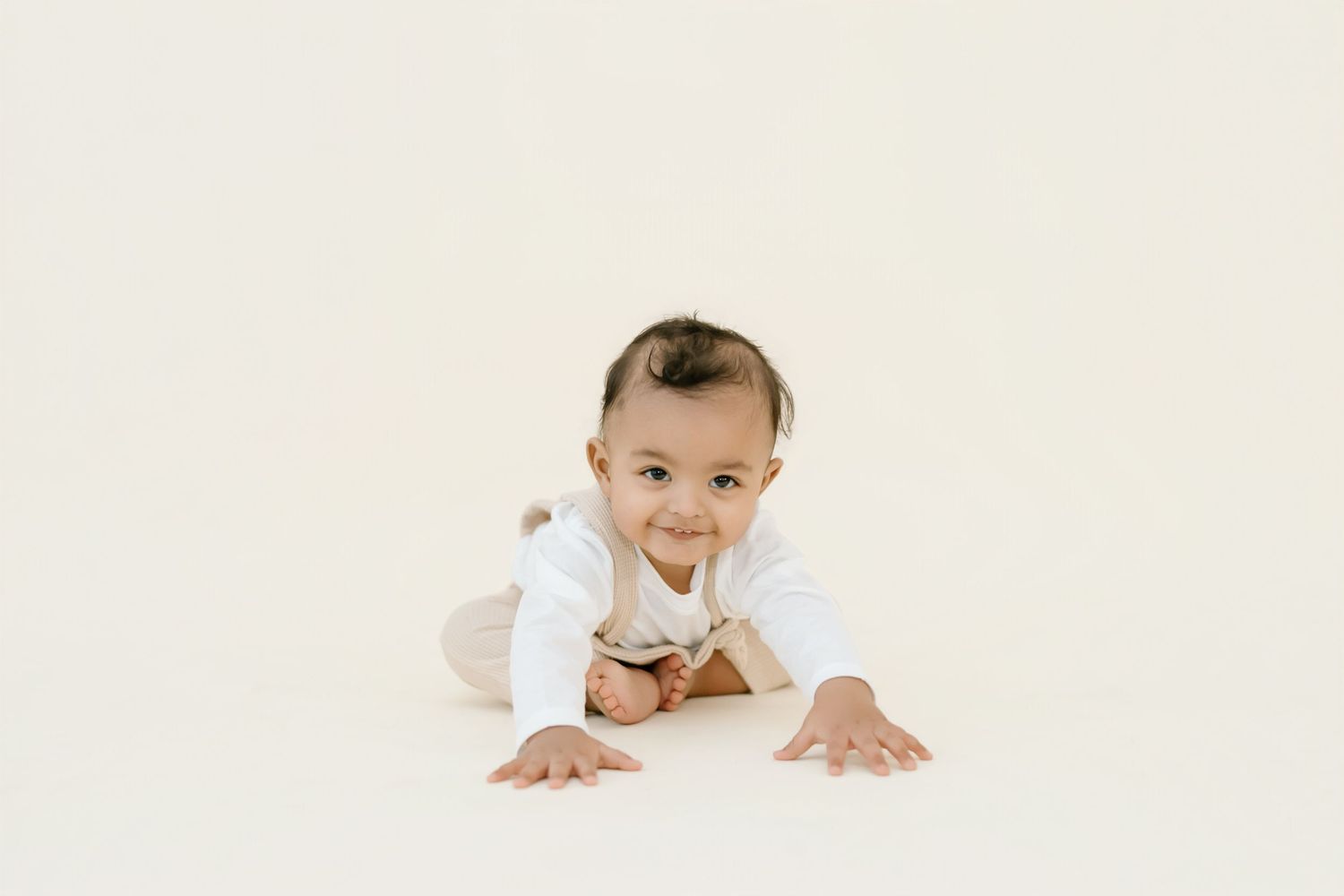 Baby in white onesie crawling and smiling on white background.