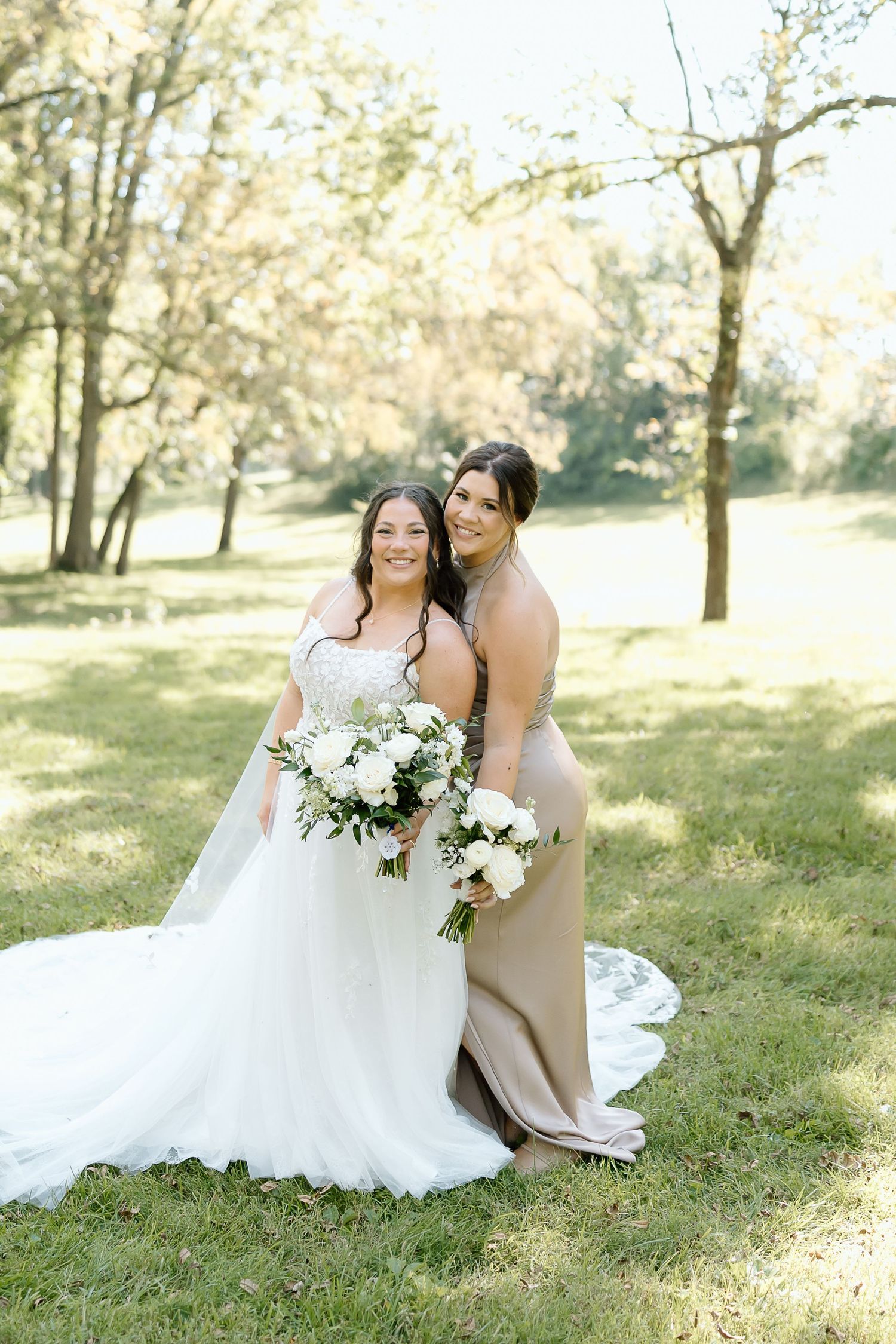 A romantic outdoor wedding photo session in a sunlit park with white floral bouquets and flowing dress details.