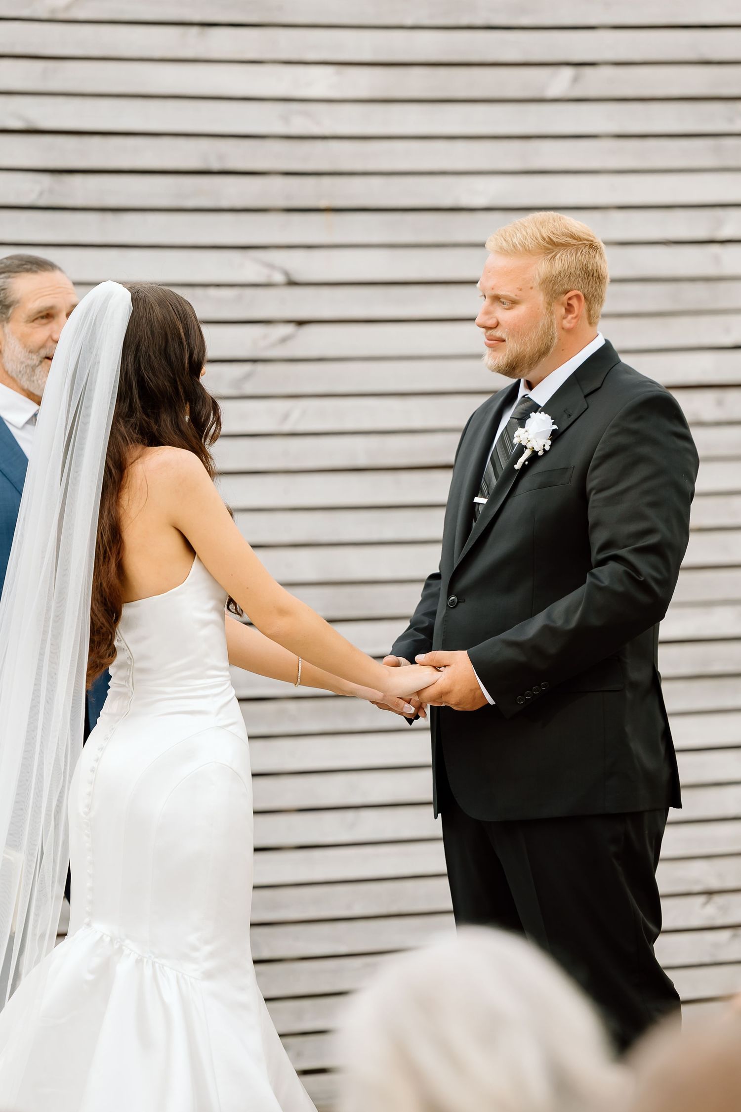 A sequence of wedding photos showing a couple exchanging rings during their outdoor ceremony against a white wall.