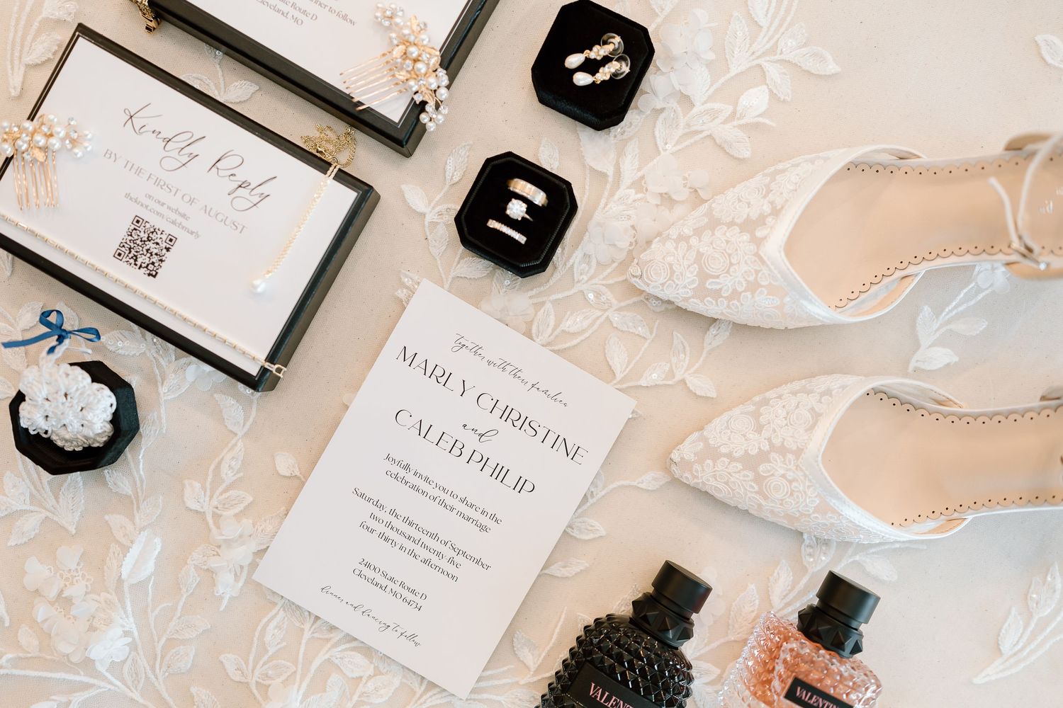 Wedding details flatlay with invitation, high heel shoes, perfume bottles and jewelry on white lace background.