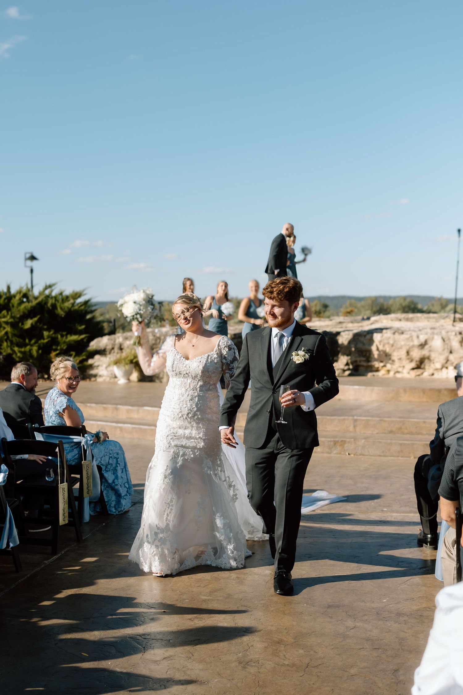A wedding couple celebrates with guests during an outdoor ceremony at a scenic coastal location during sunset.