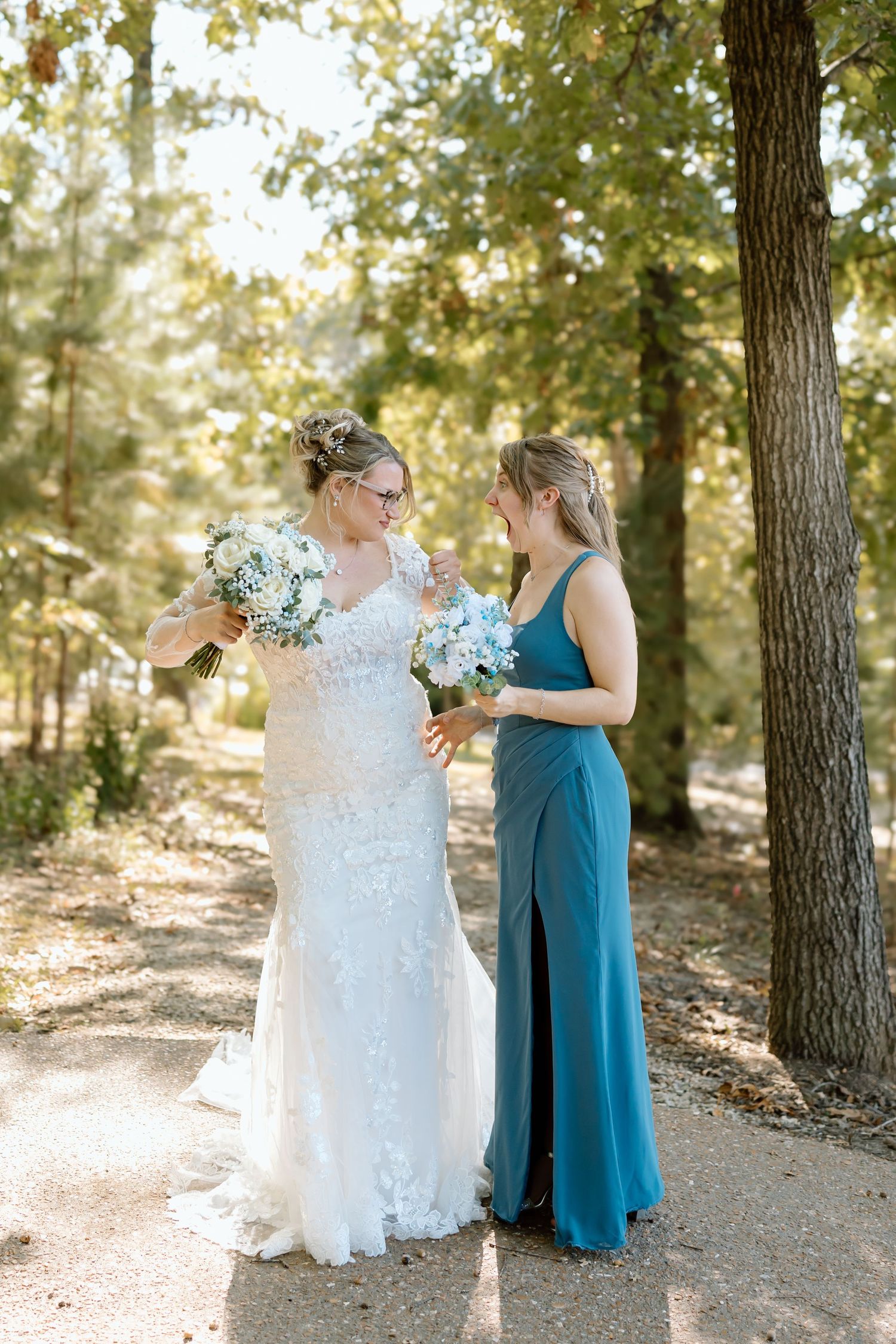 Two people in wedding attire share a joyful moment together in a sunlit forest setting.