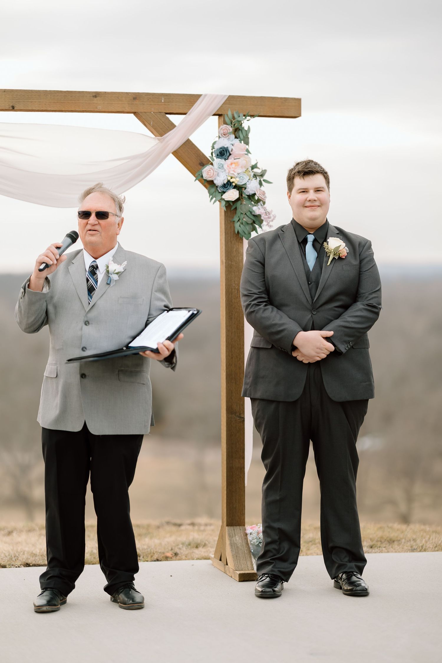 Groomsmen in matching gray and black suits pose playfully in sequence at an outdoor wedding venue.
