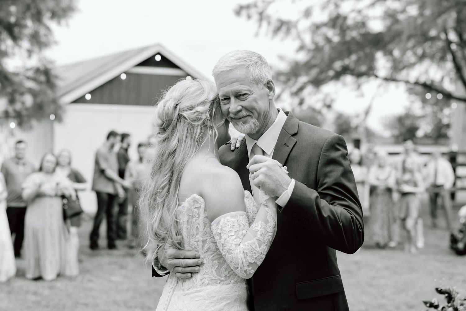 Father and bride share emotional first dance at outdoor wedding reception in black and white photo.