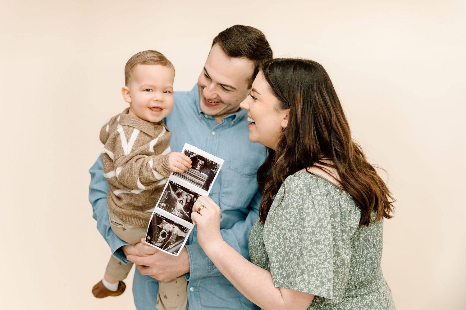 Happy family holding ultrasound photos and embracing while sharing joyful pregnancy announcement moment.