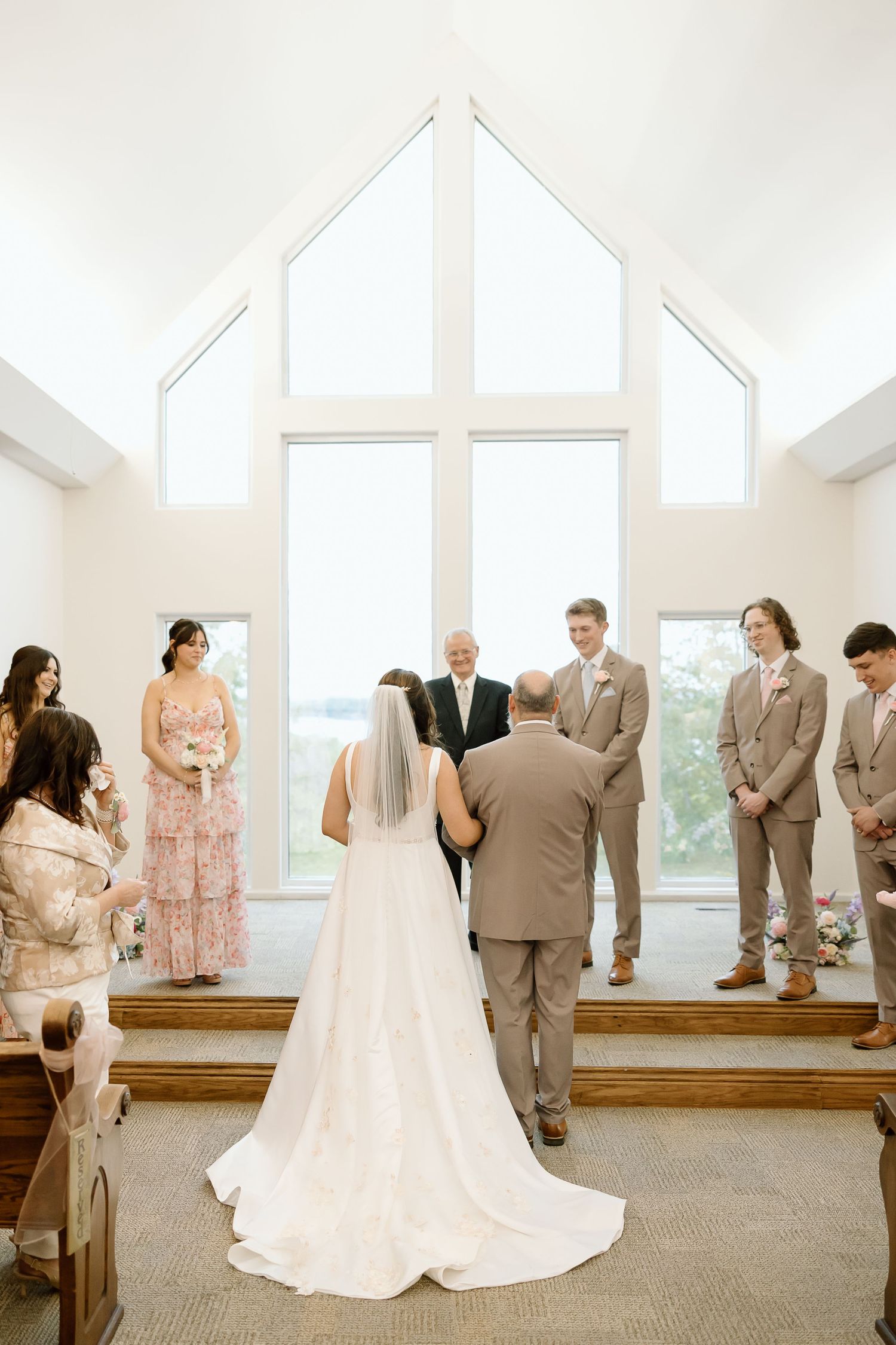 A wedding ceremony takes place in a bright chapel with vaulted ceilings and large windows overlooking scenic views.