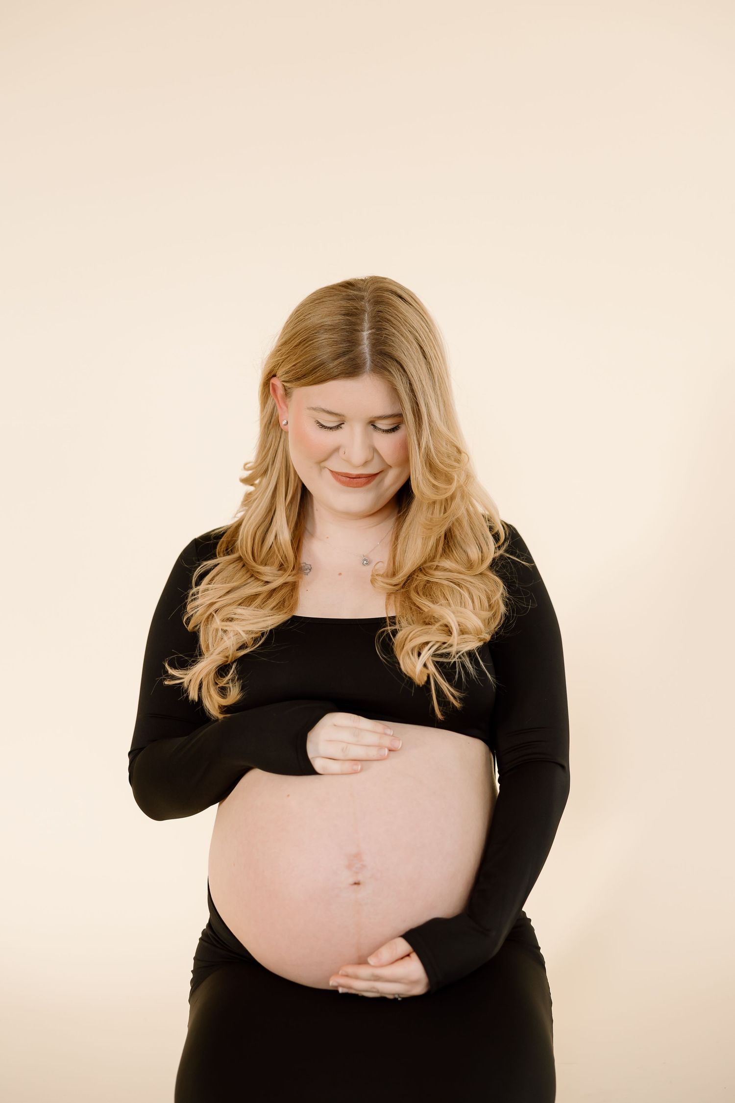 A pregnant woman in a black top poses for a maternity photo against a light background.