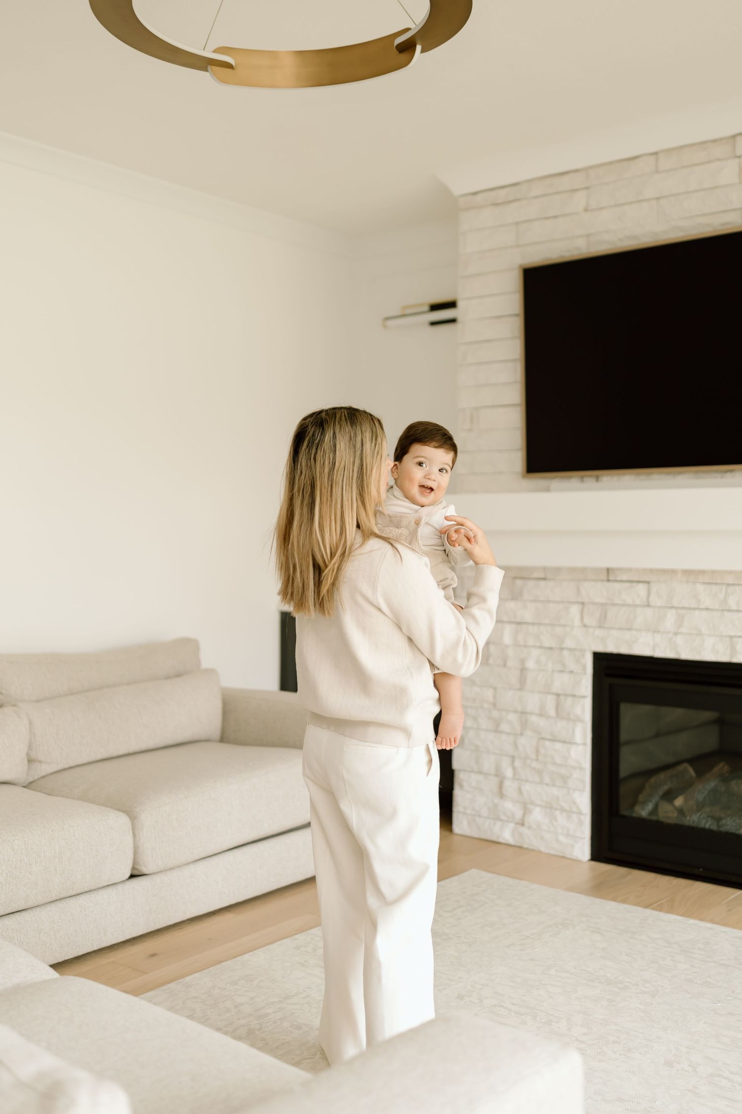A cozy modern living room features a white brick fireplace, plush sofa, and circular gold light fixture overhead.