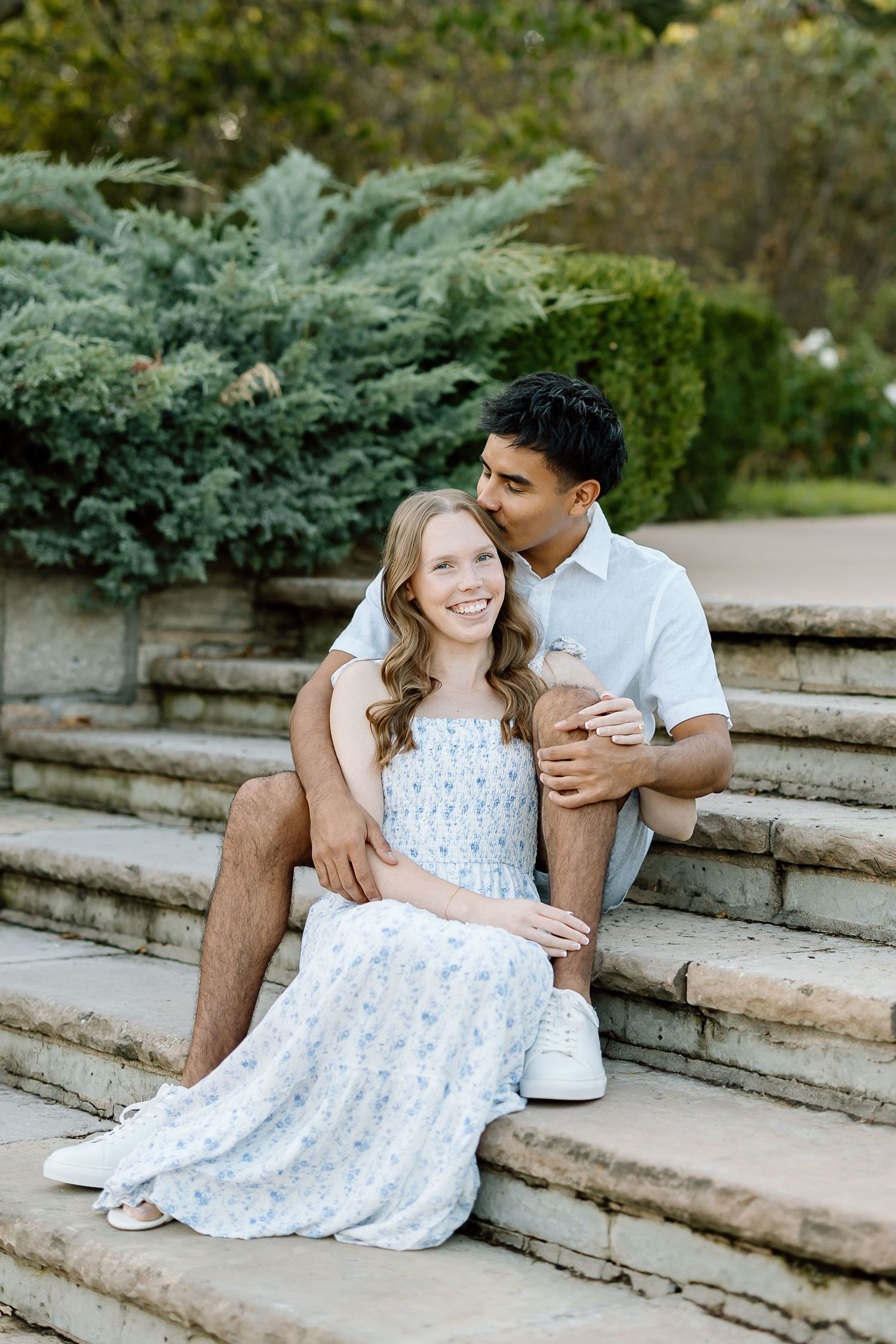 A romantic couple sits together on stone steps in a garden setting, sharing intimate moments in a series of photos.