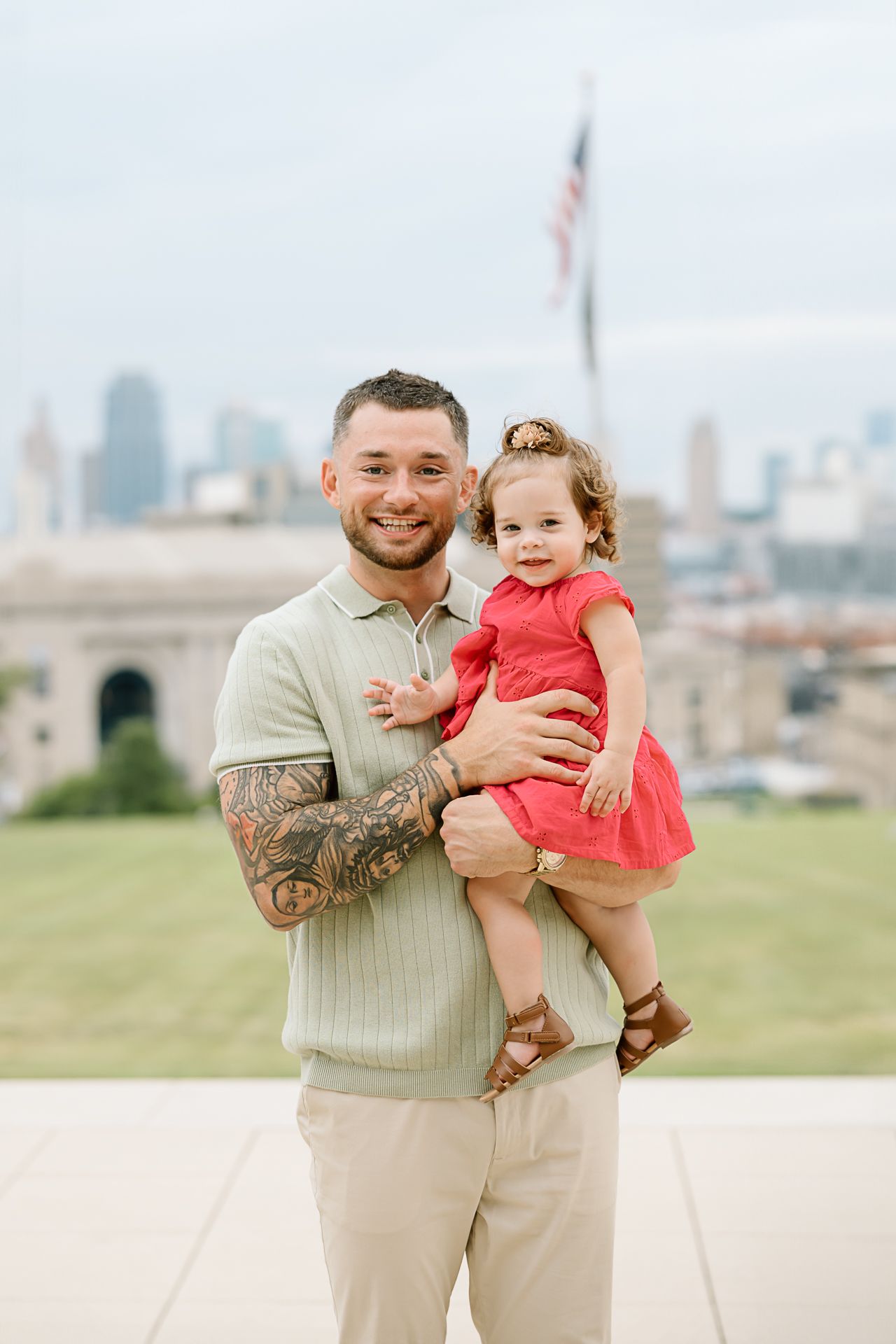 A parent and child share a joyful moment together against a city backdrop on a sunny day.