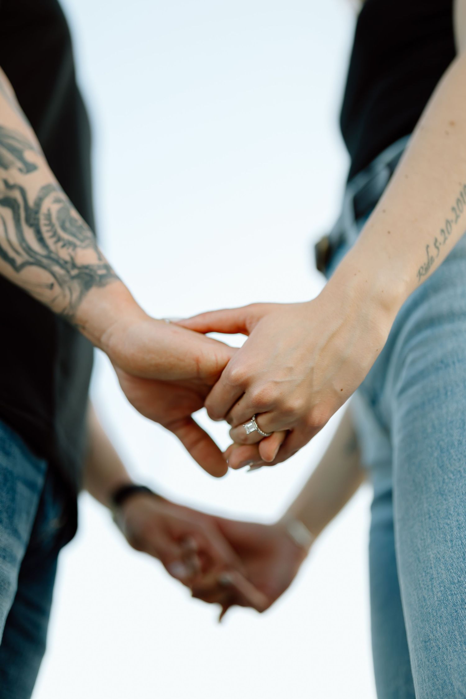 Close-up view of tattooed hands holding together against a light background.