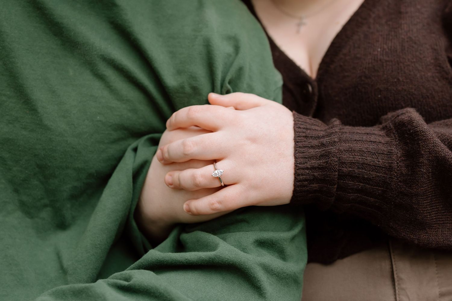 Close-up detail of hands wearing green and brown sweaters against a neutral background.