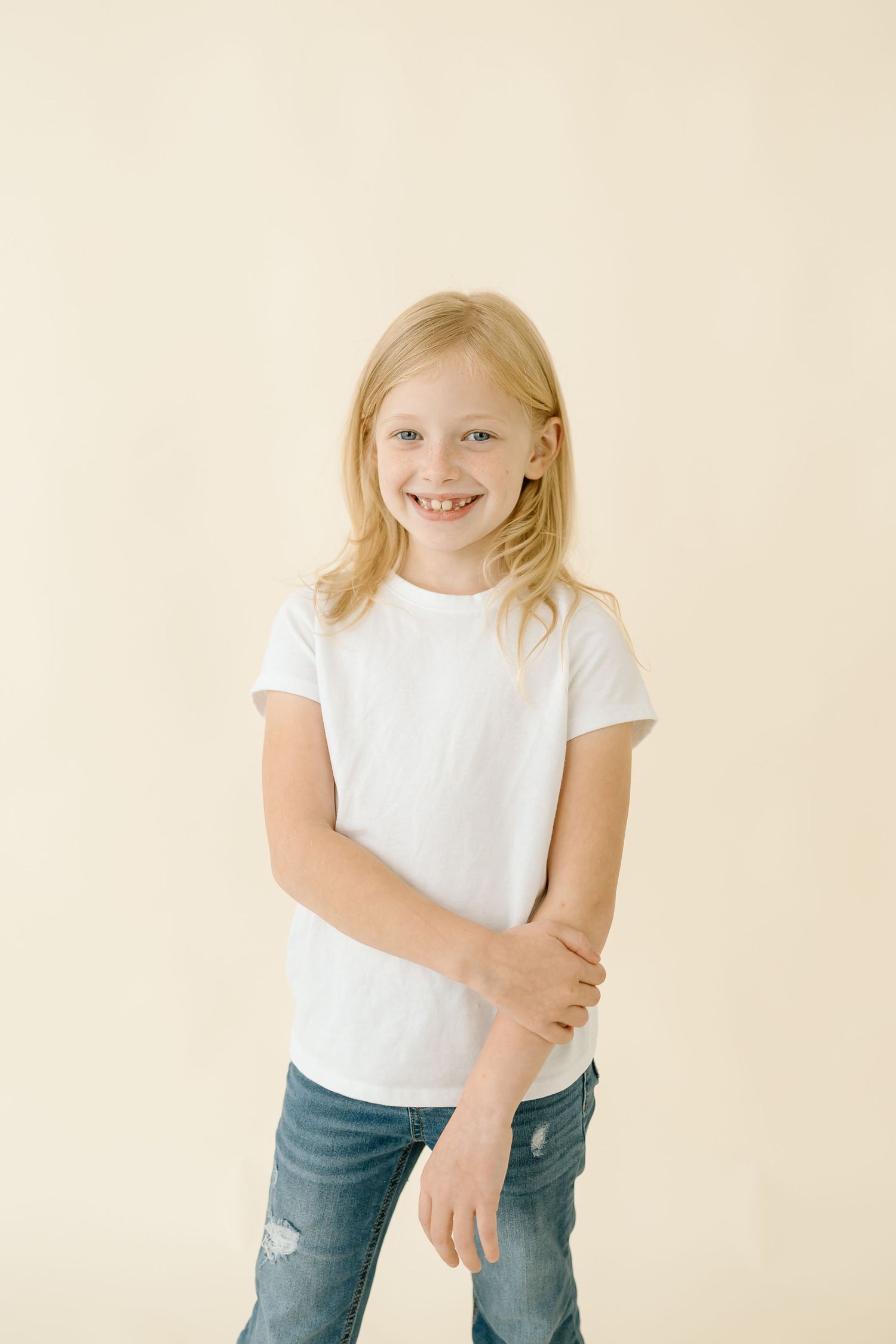 A child in a white t-shirt and jeans poses playfully against a cream-colored backdrop.