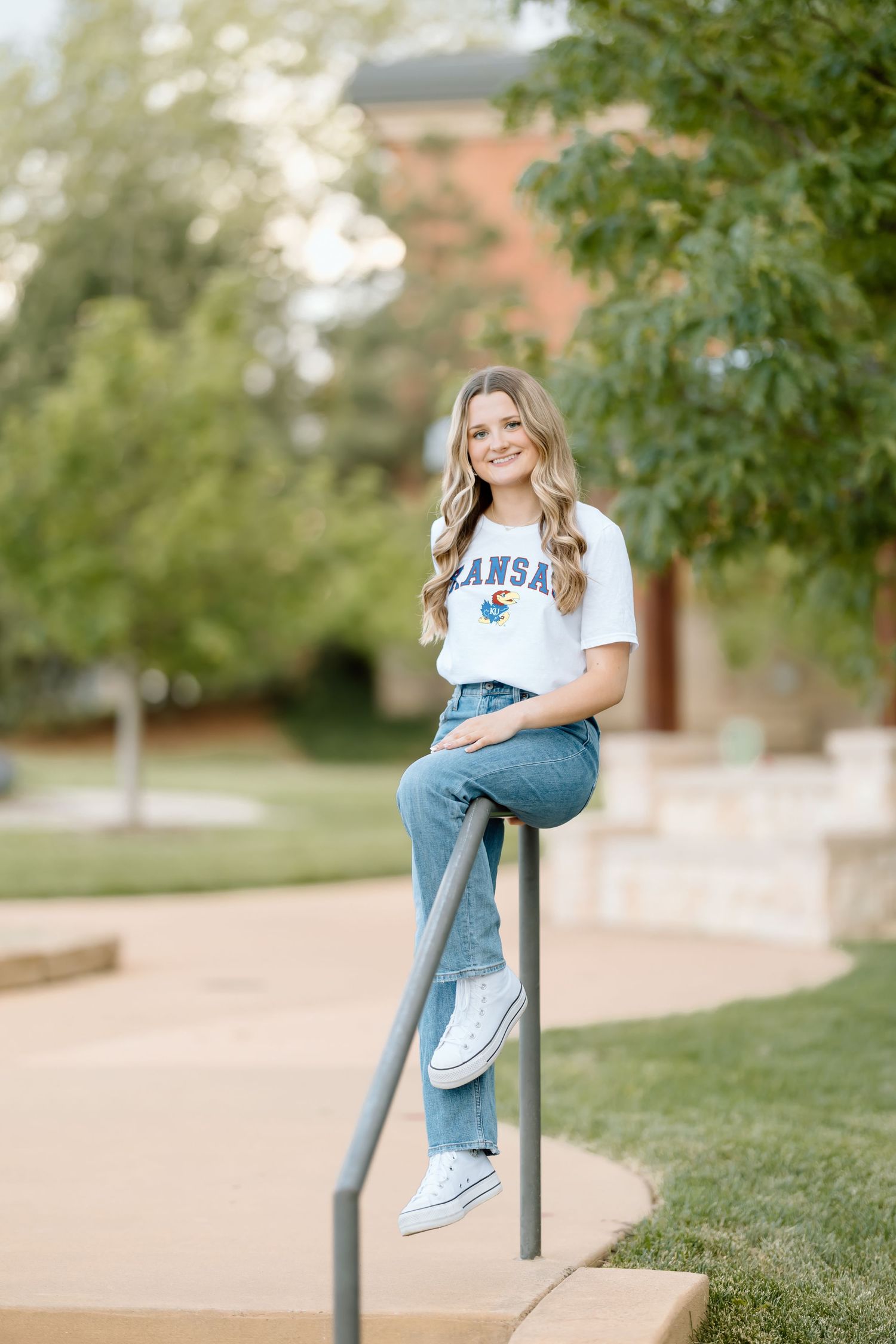 A person wearing jeans and a white t-shirt poses casually on outdoor railings in a university campus setting.