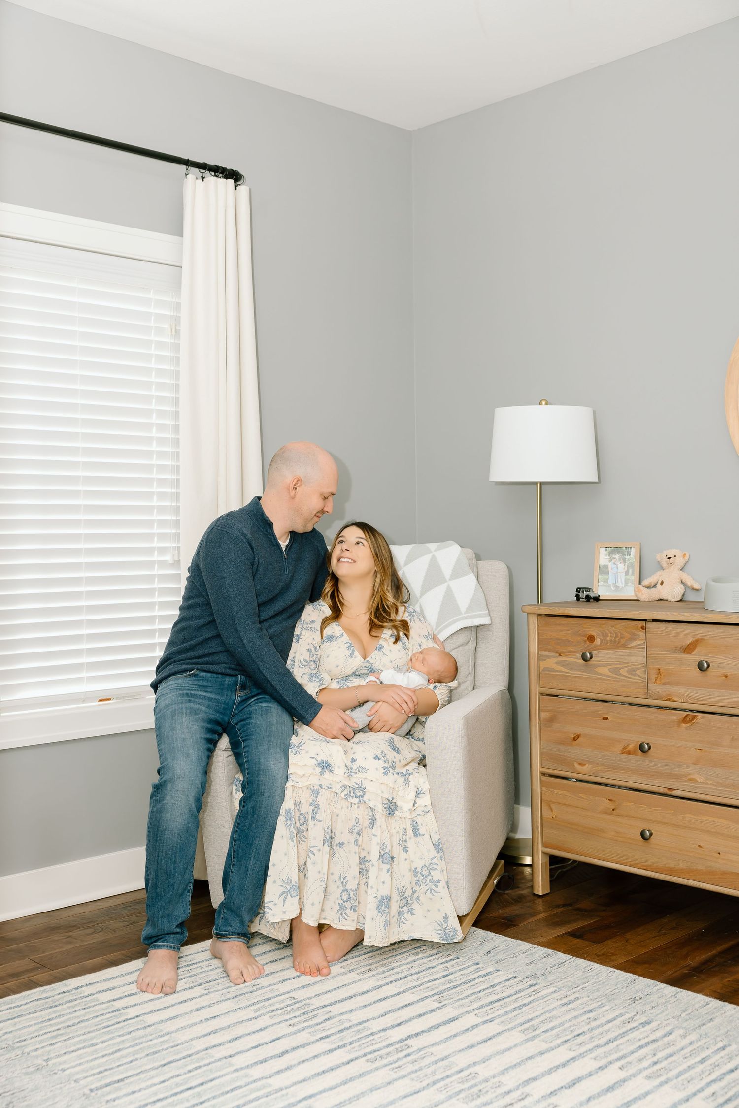 A family shares tender moments together in a bright bedroom with wooden furniture and white curtains.
