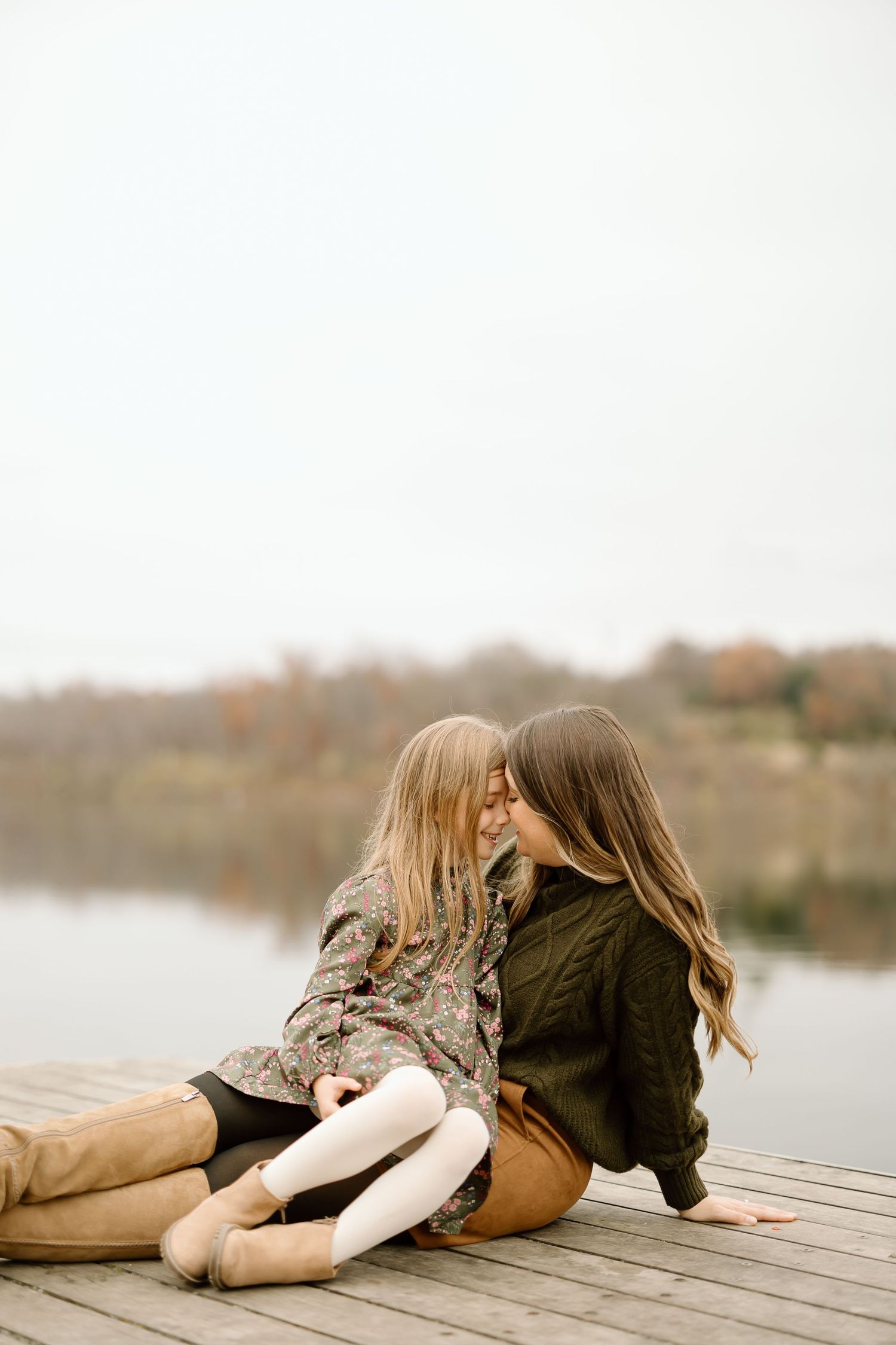 Intimate family moment captured on wooden dock with lake backdrop during fall season.