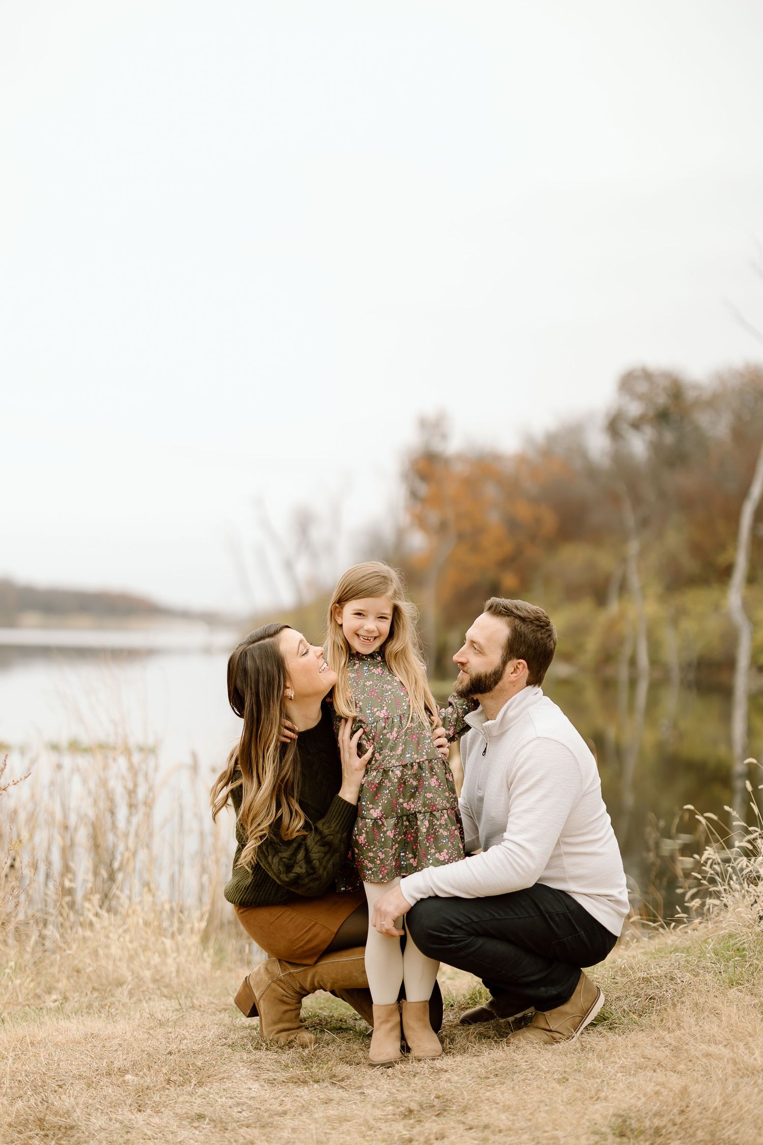 Candid family moment captured near lake during fall season photoshoot.