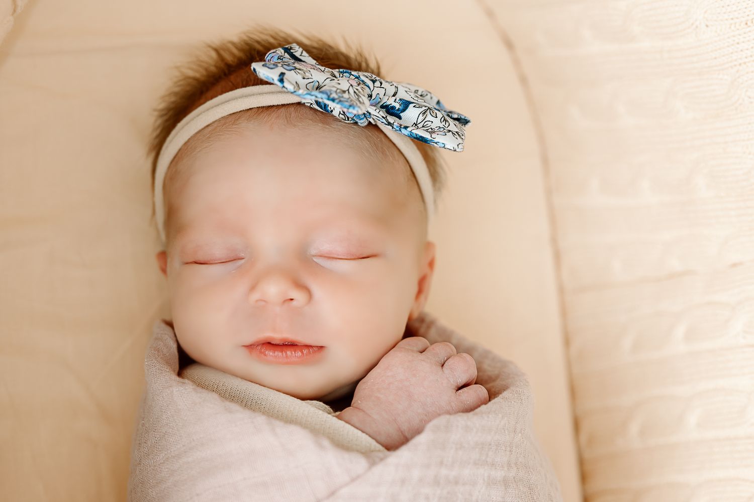 Sweet newborn portrait with sparkly bow headband and soft white swaddle.