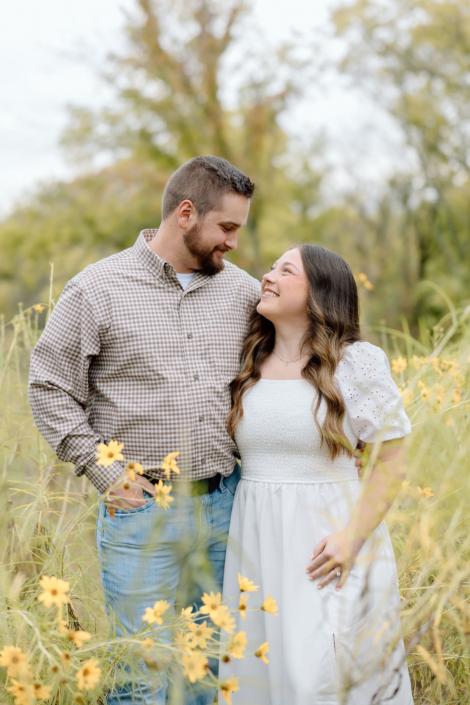 A couple laughs together while standing in a field of yellow wildflowers.