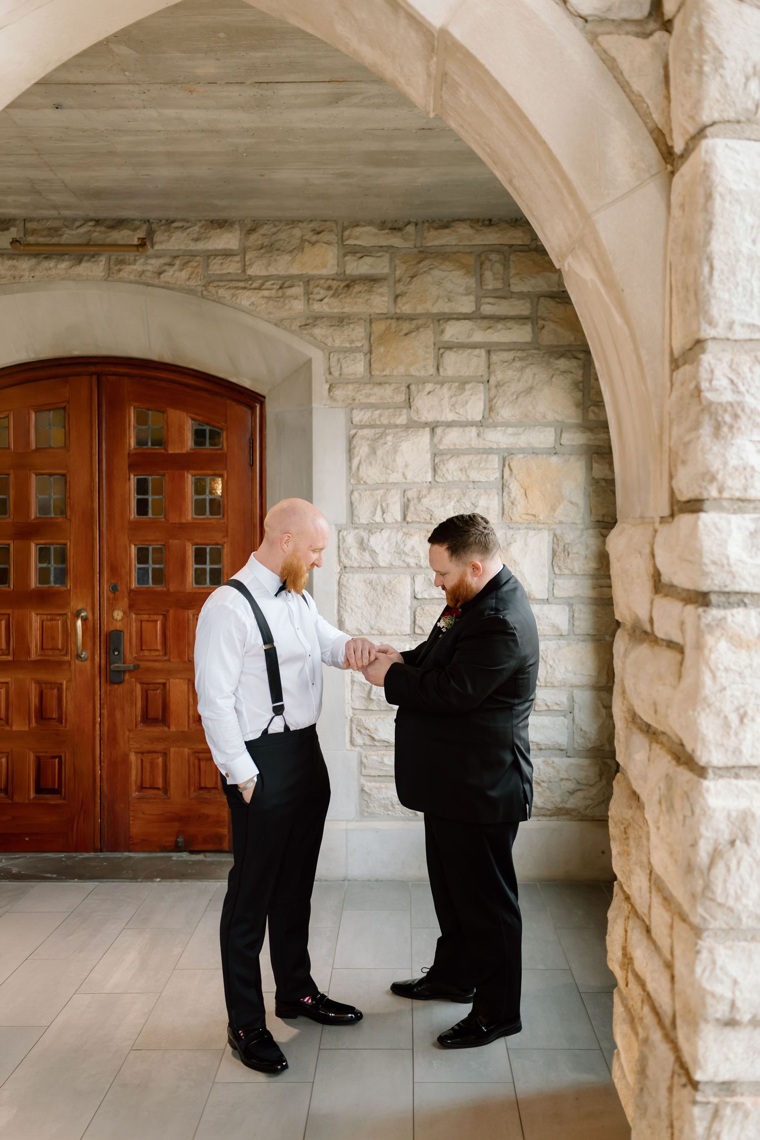 Two people in formal attire share an emotional moment under stone archways in a historic building hallway.