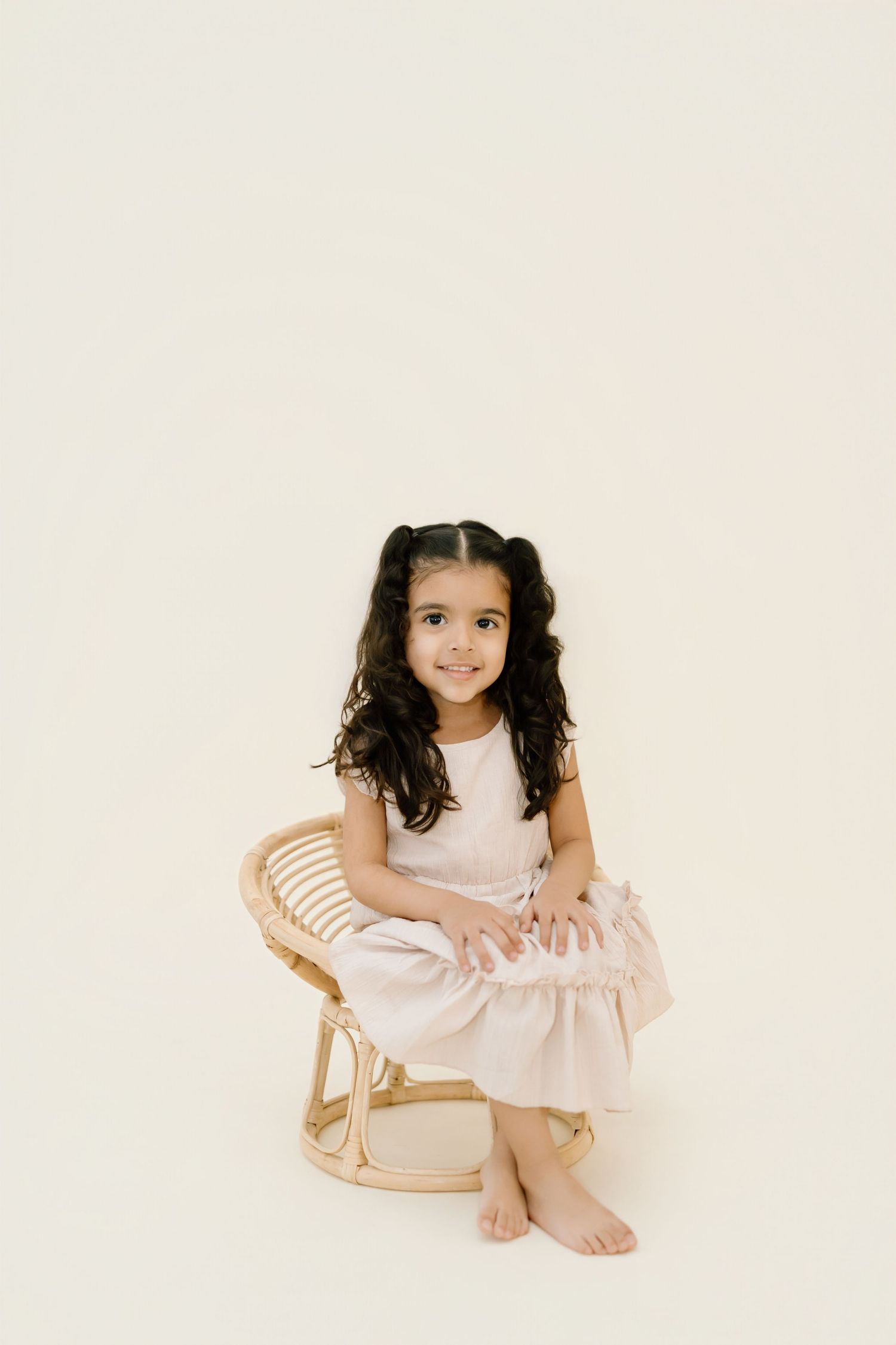 A young child in a light-colored dress poses on a cream background in a three-part photo series.