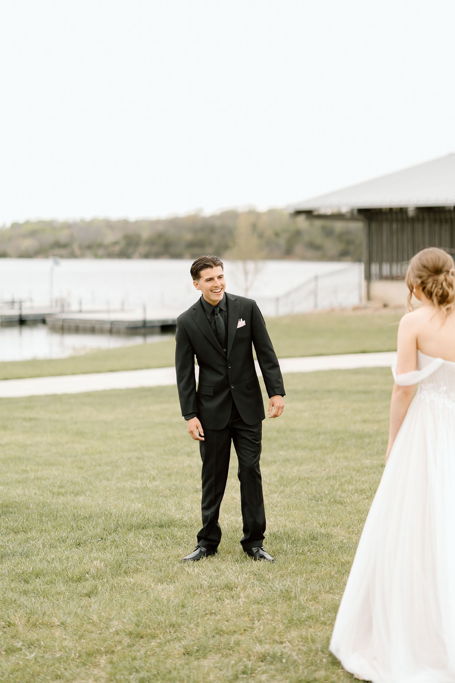 Wedding first look moment captured outdoors by a lake with couple in formal attire.