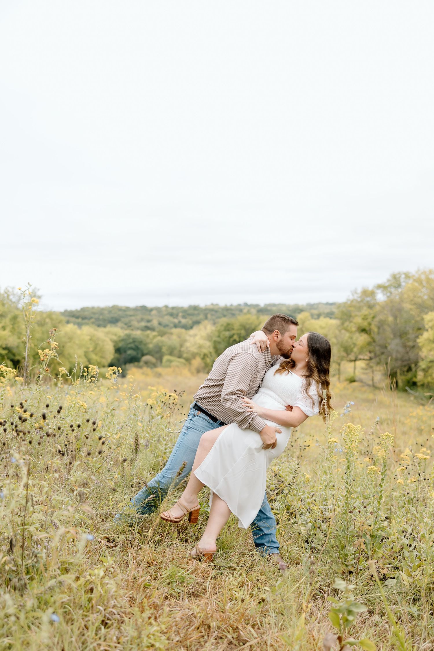 Playful couple dips in romantic pose surrounded by prairie wildflowers.