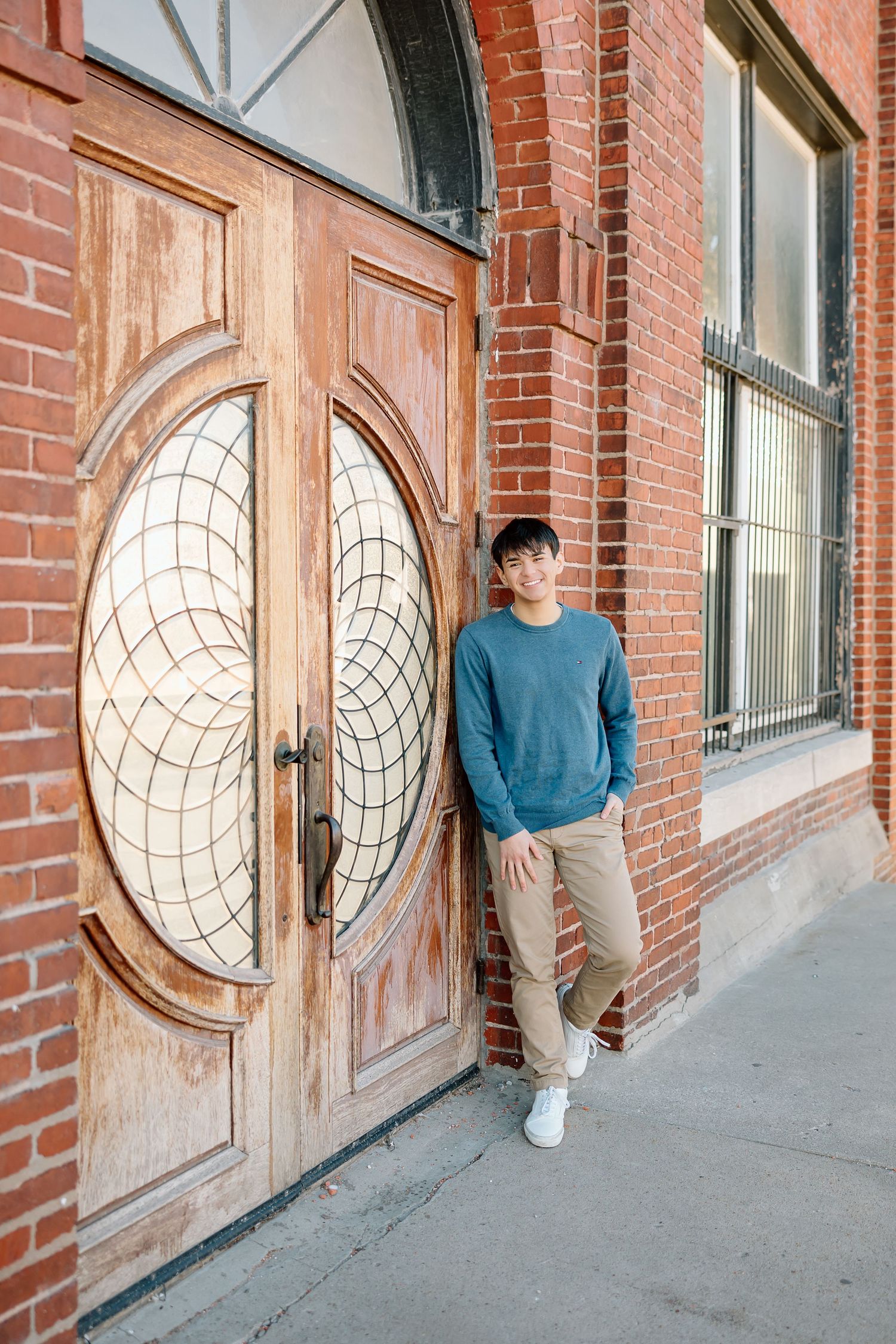 Casual portrait by vintage wooden door with circular geometric pattern in brick building.