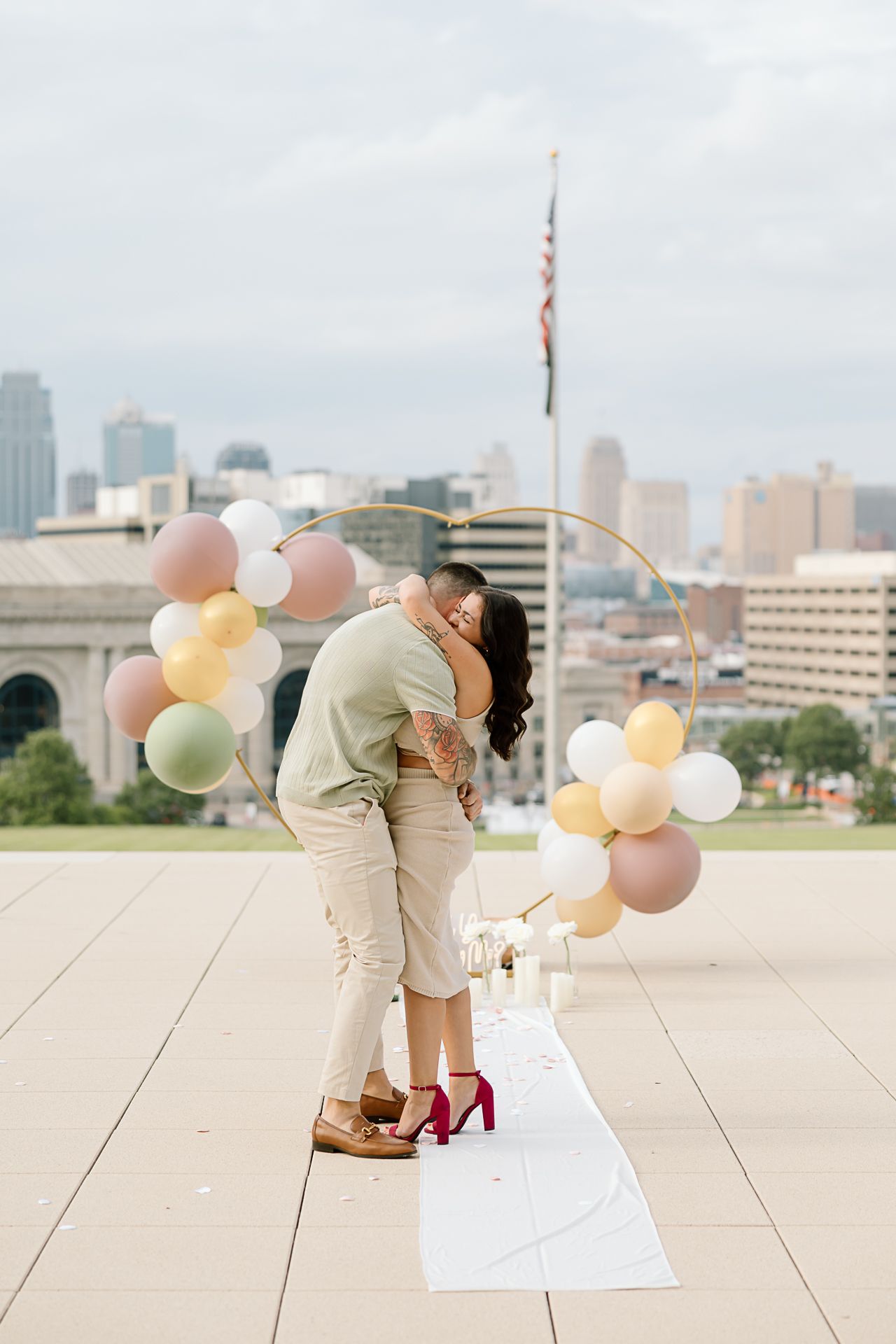 A romantic proposal scene on a rooftop with pastel balloons and the city skyline in the background.