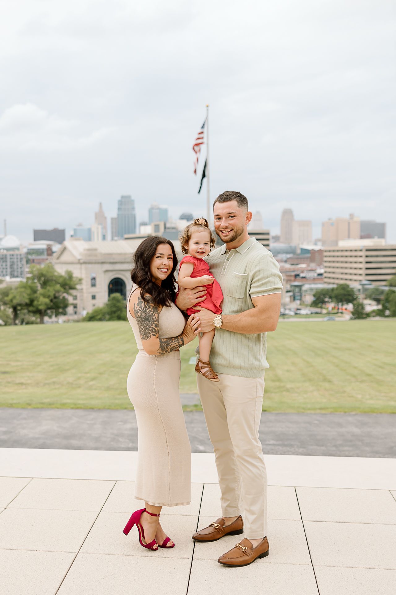 A happy family shares a tender moment together on a grassy hill overlooking a city skyline.