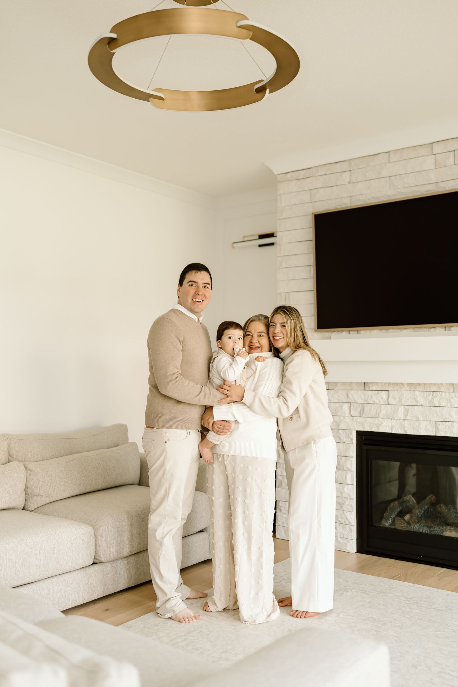 A group in white clothing stands together in a modern living room with a white brick fireplace and mounted TV.