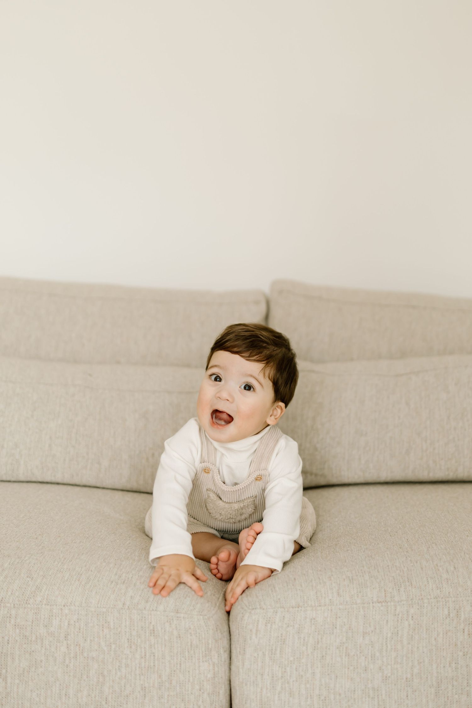 A baby in a white top sits on a light gray couch showing different playful expressions in a series of photos.