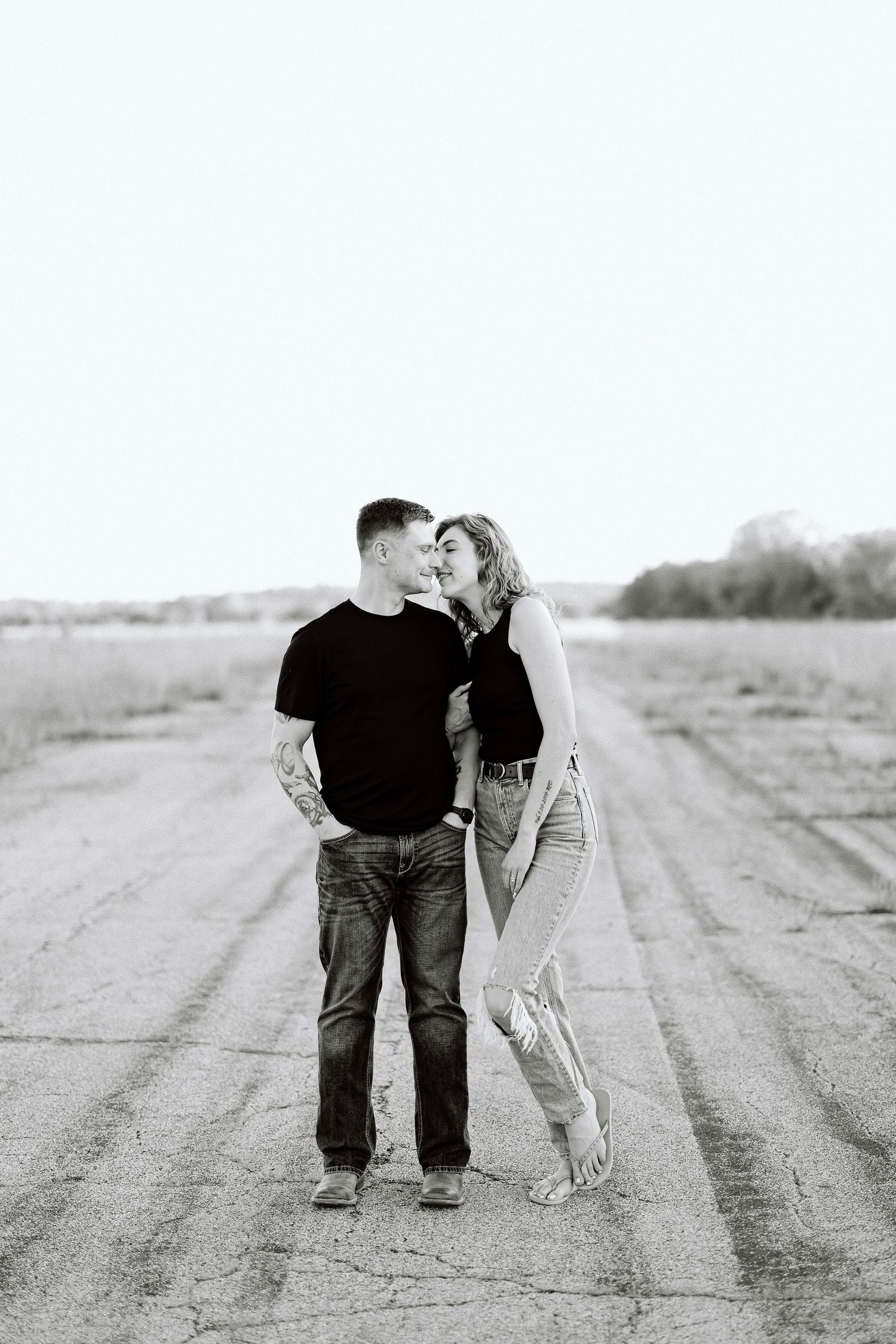 A couple shares an intimate moment on a dirt road in a black and white photograph.