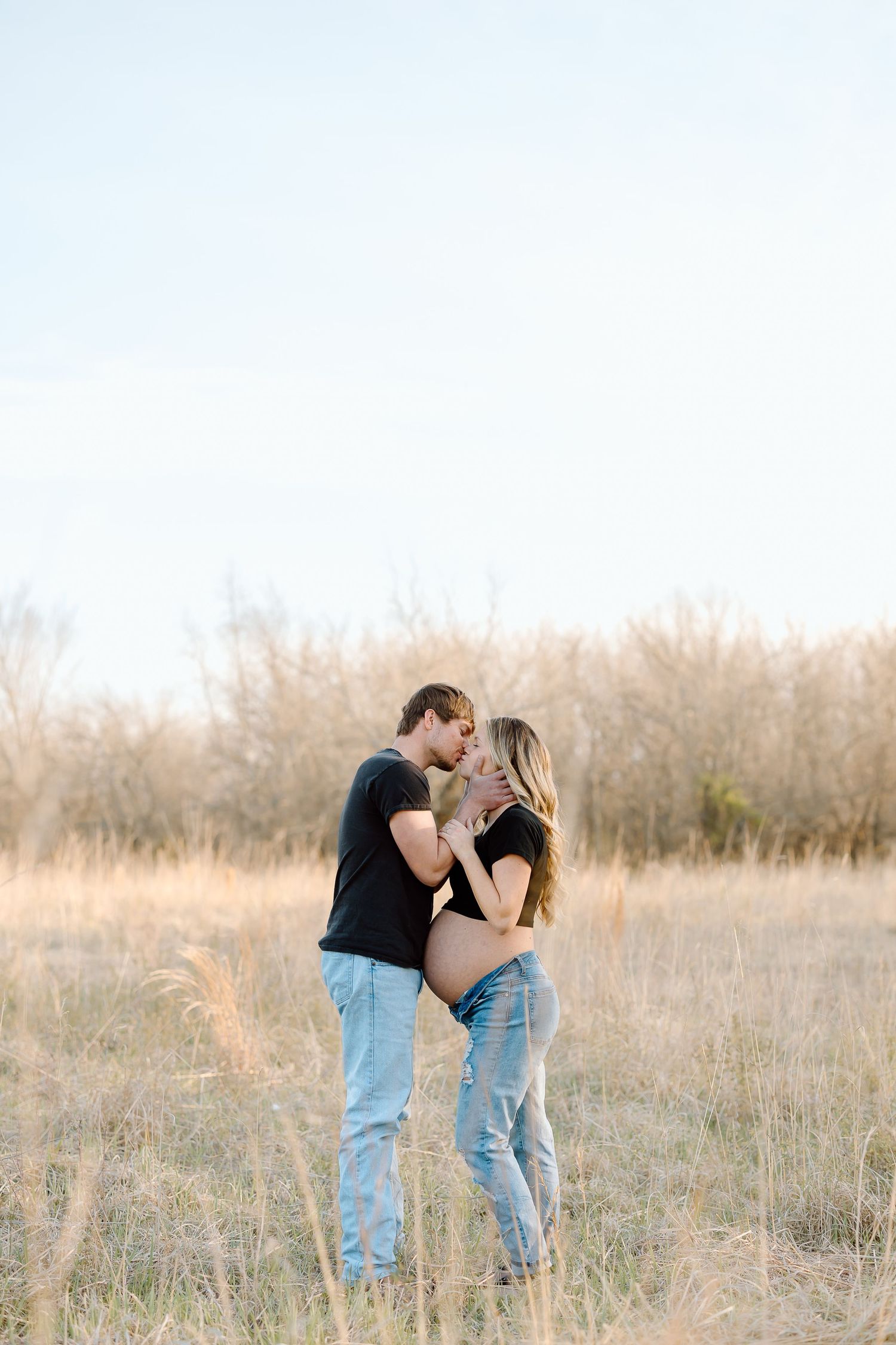 A couple shares a romantic moment together in a sunlit field of tall grass during golden hour.