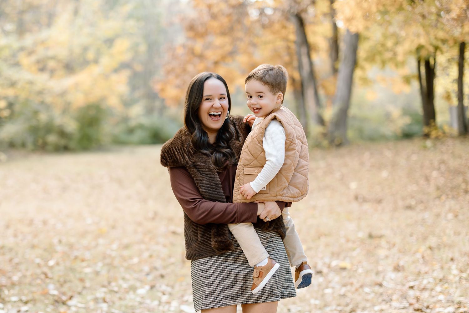 Parent and child share joyful moments together while playing in autumn leaves during a fall photo session.