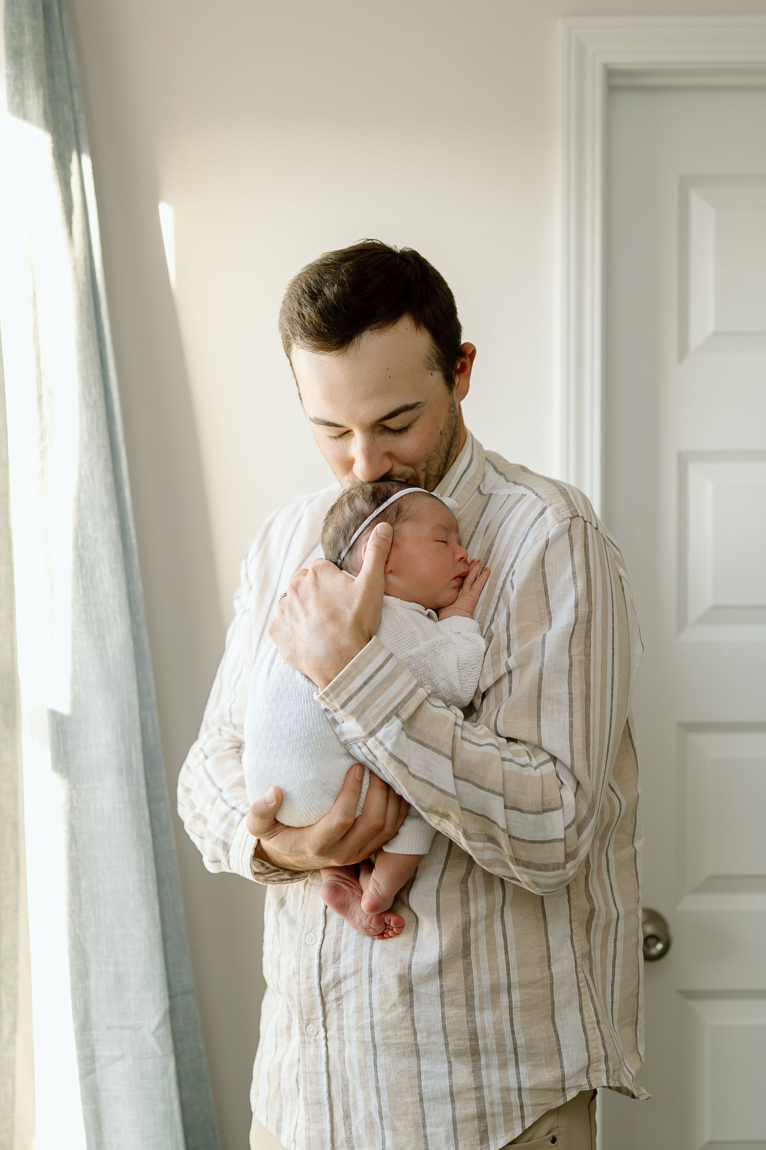 A series of tender moments between a parent and baby in a bright white room with striped shirt and soft lighting.