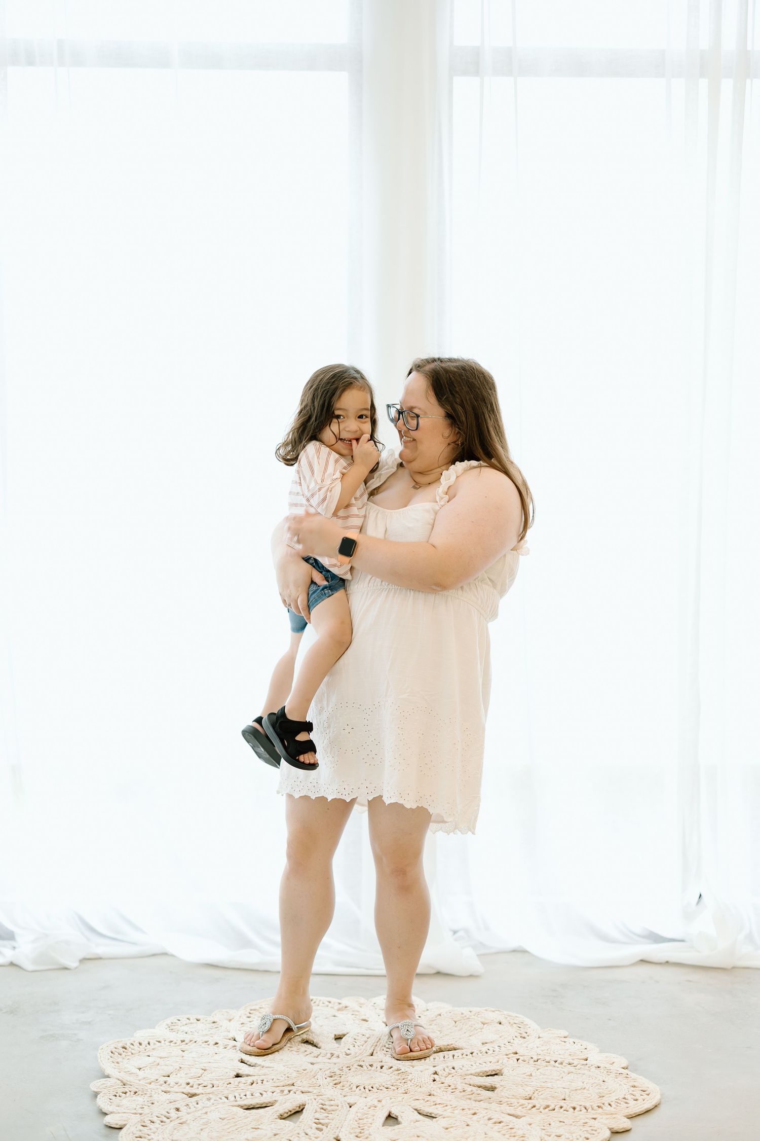 A tender moment between parent and child standing on a circular rug in a bright white room.