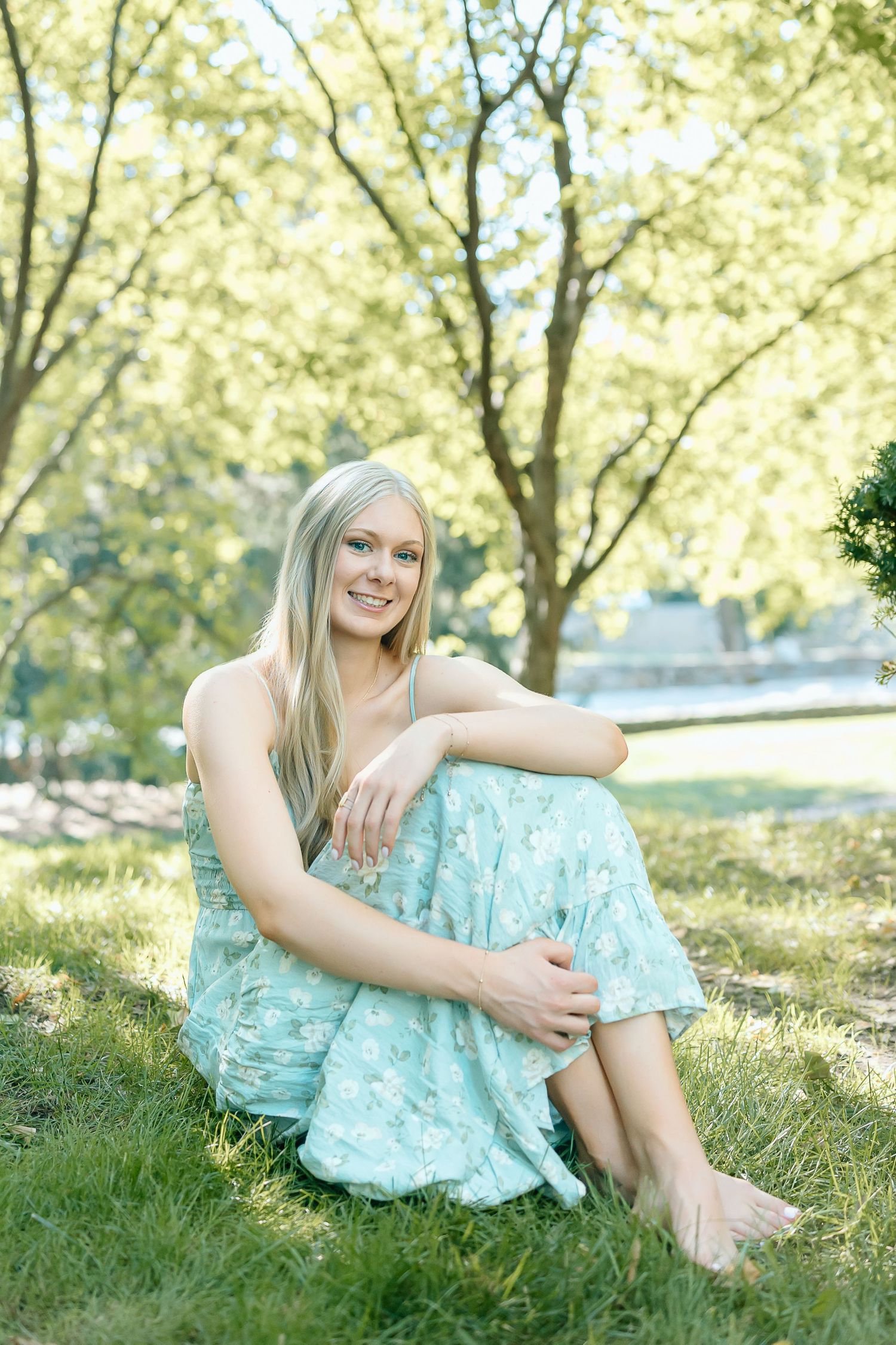 A person in a light turquoise sundress relaxes on a grassy hill during a sunny summer day.