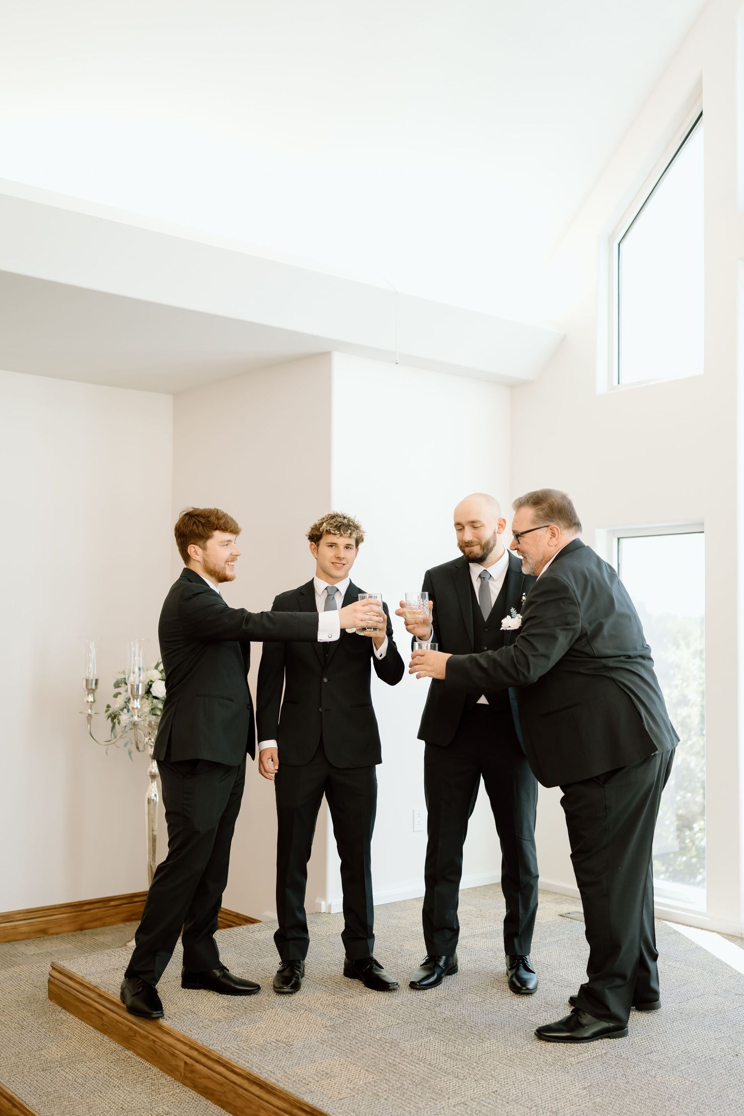 Four groomsmen in black suits share a lighthearted moment while getting ready before a wedding ceremony.