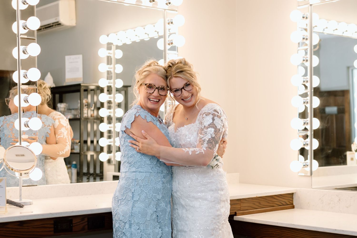Two people share an emotional moment while getting ready in a dressing room with bright vanity lights.