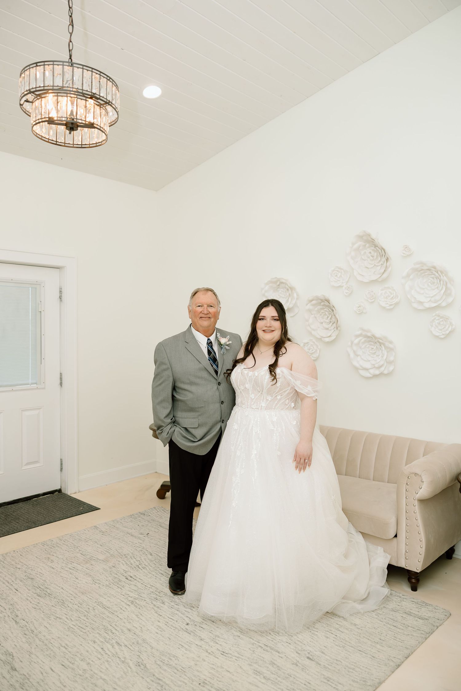 A bridal suite interior with crystal chandelier lighting and elegant white decor features a plush velvet bench seating area.