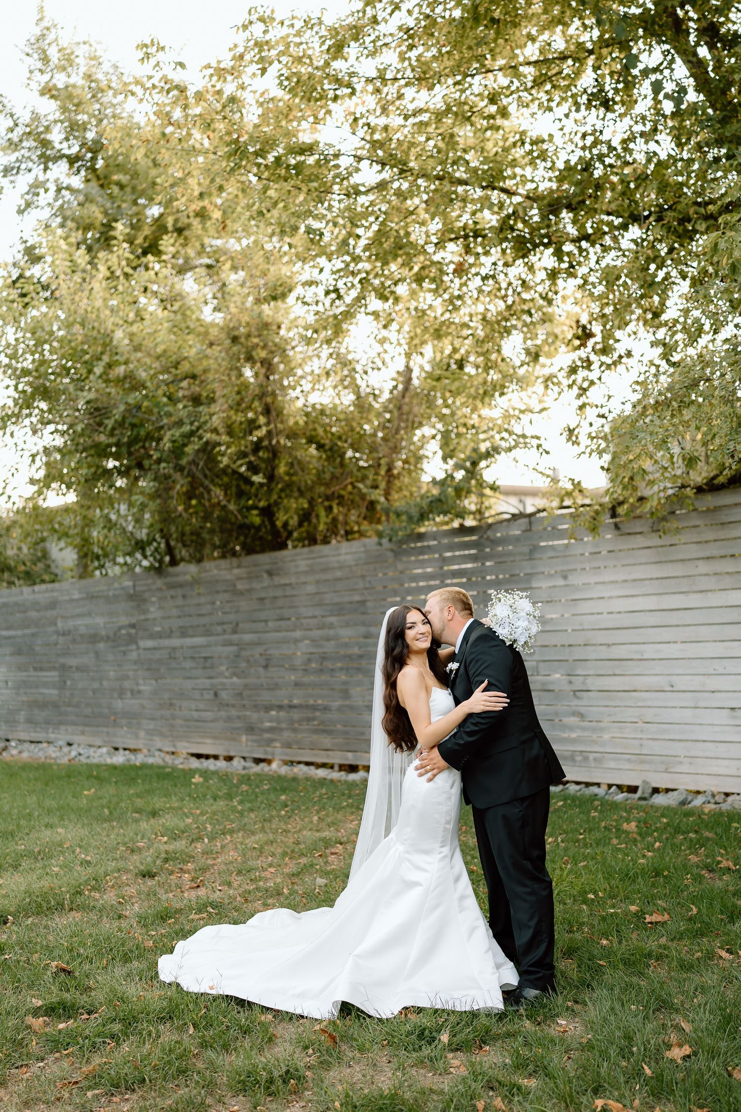 A romantic wedding couple shares intimate moments against a rustic gray wall in an outdoor garden setting.