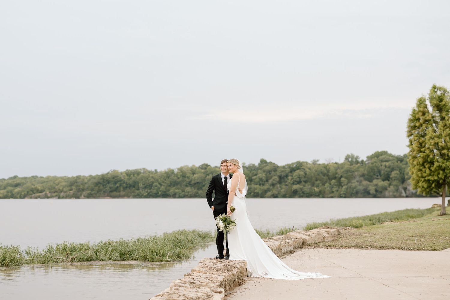 Wedding party stands on sandy beach with scenic views of lake and greenery in Minnesota.