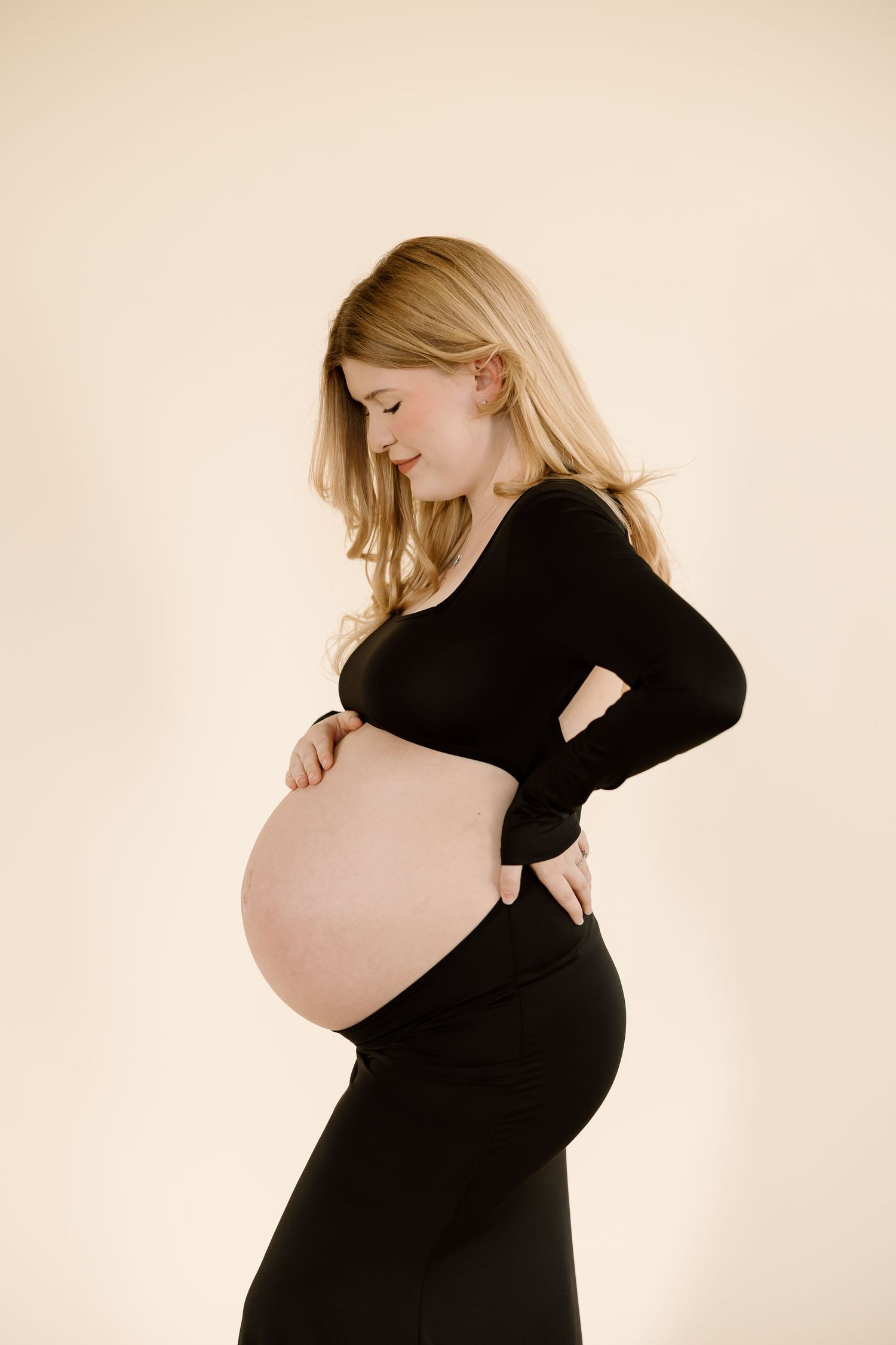 Side view maternity portrait showing woman in black dress cradling baby bump.