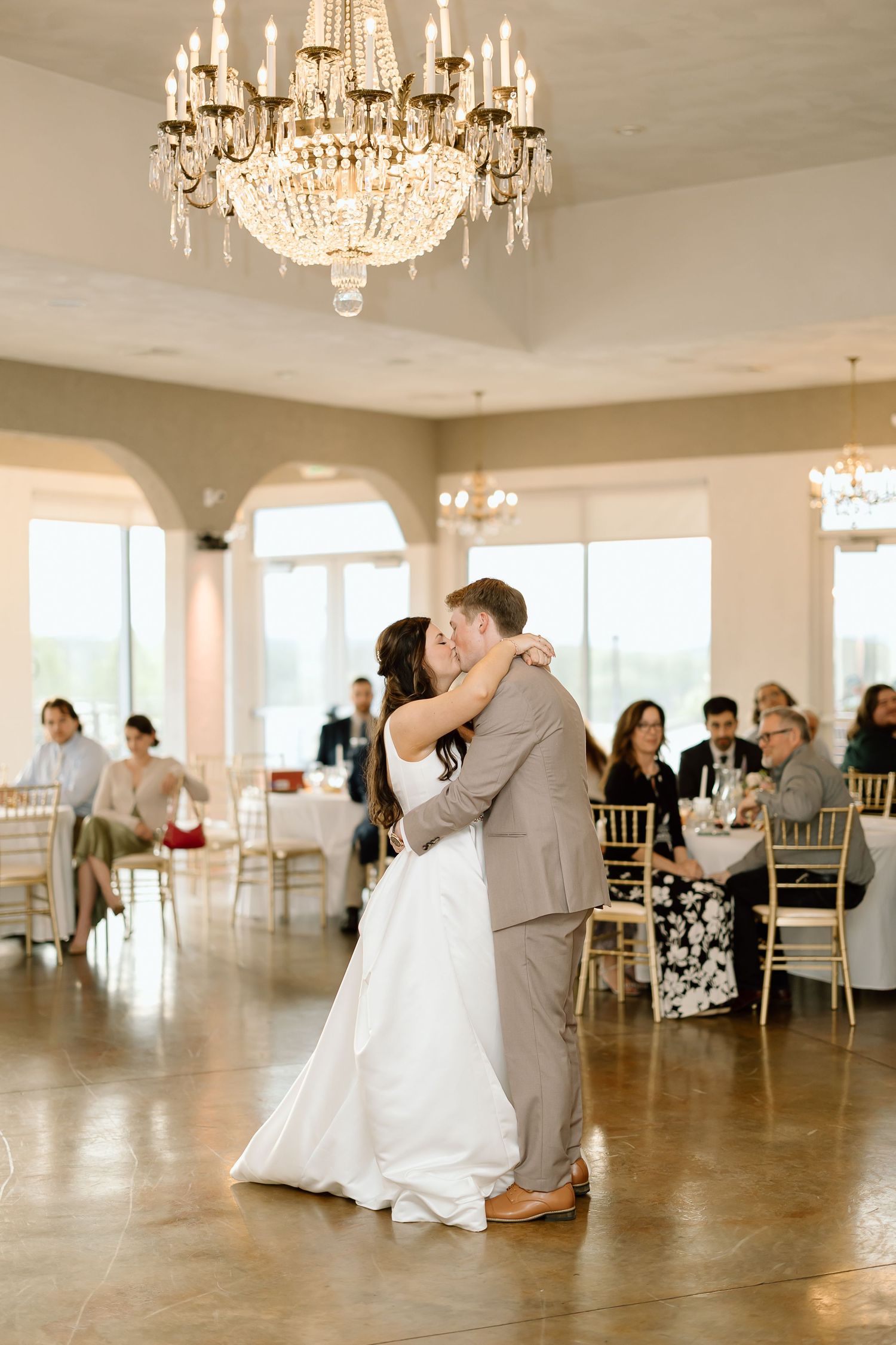 Newlyweds share first dance under crystal chandelier in elegant reception hall.