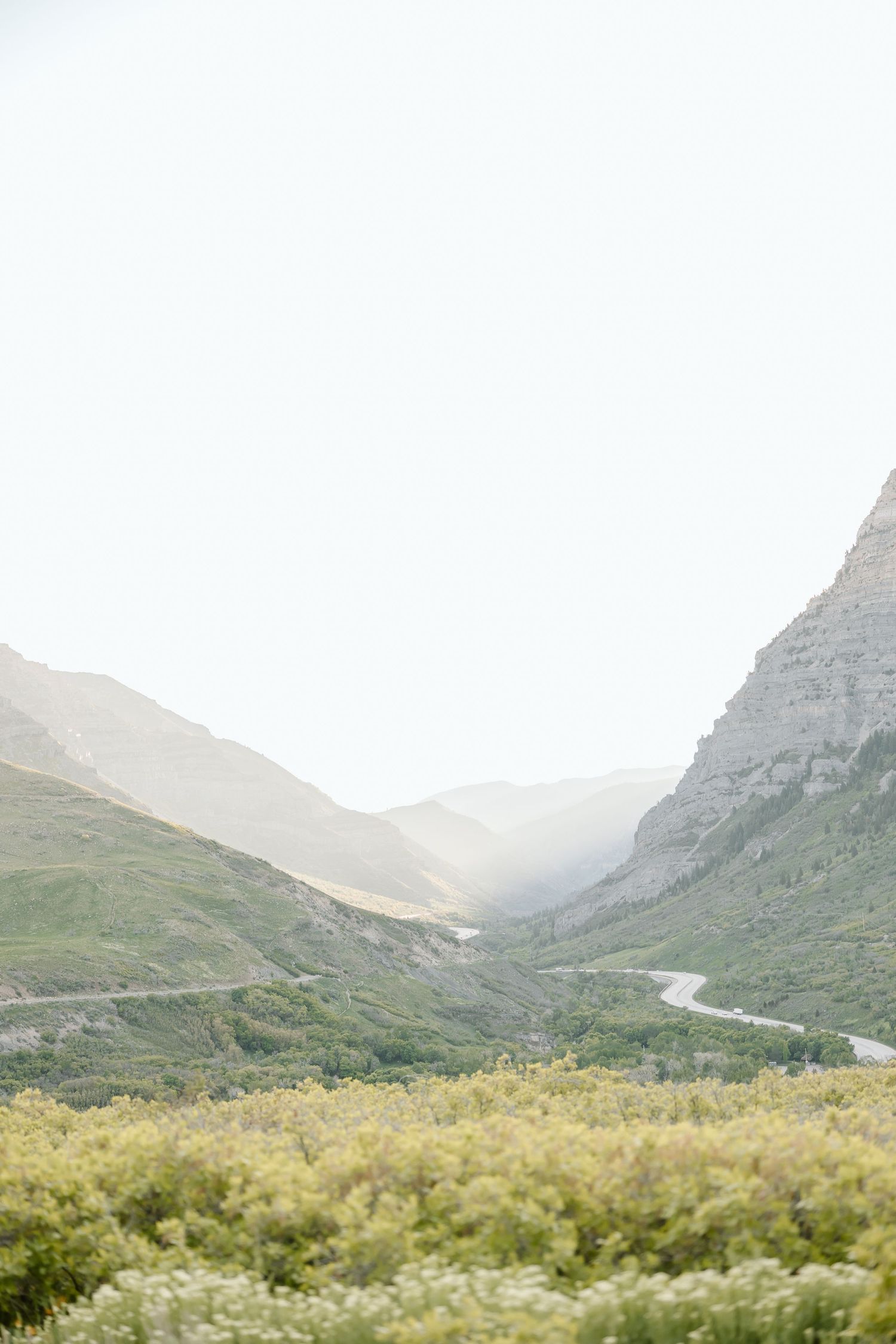 Serene mountain valley with winding road through green hillsides and misty peaks in the distance on a tranquil morning.