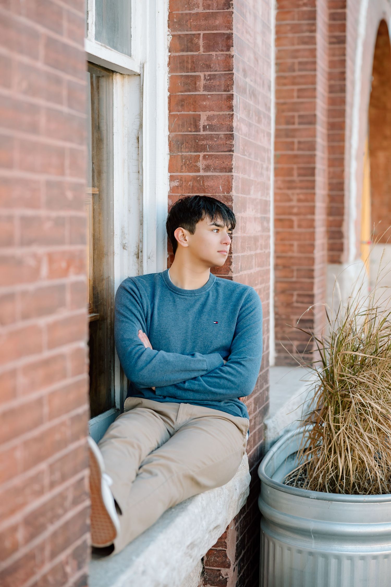 Contemplative side profile pose against brick wall with dried grass decor.