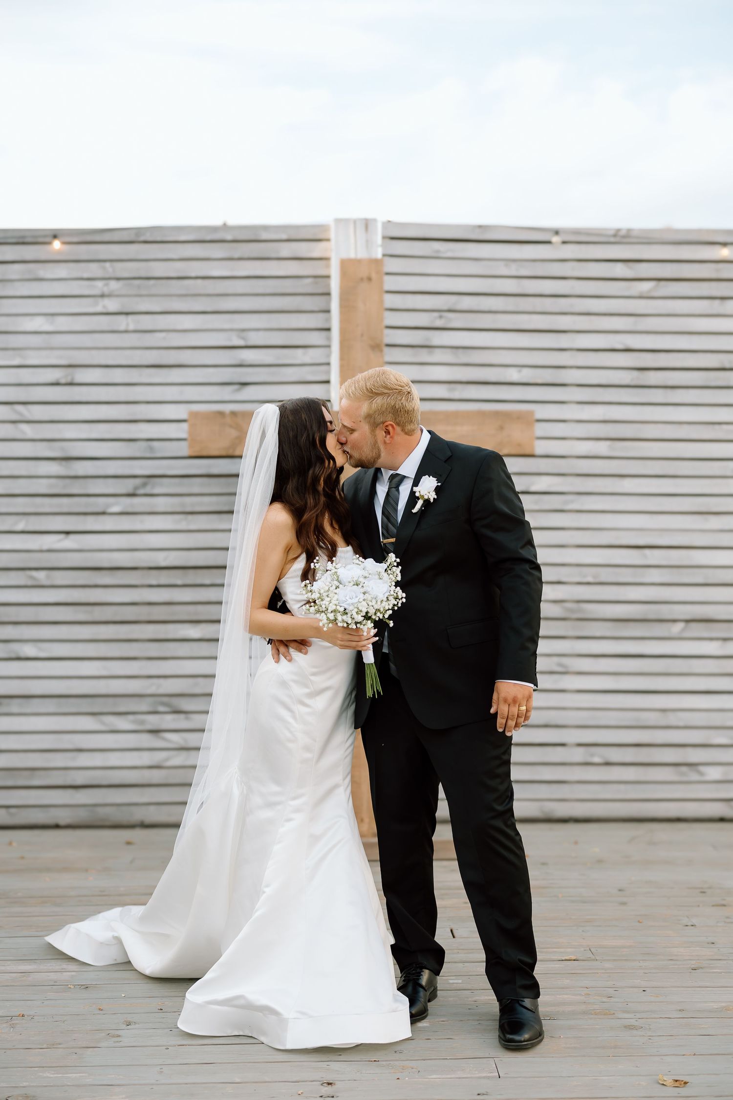 A romantic wedding couple shares intimate moments in front of a gray wooden wall in a series of connected photos.