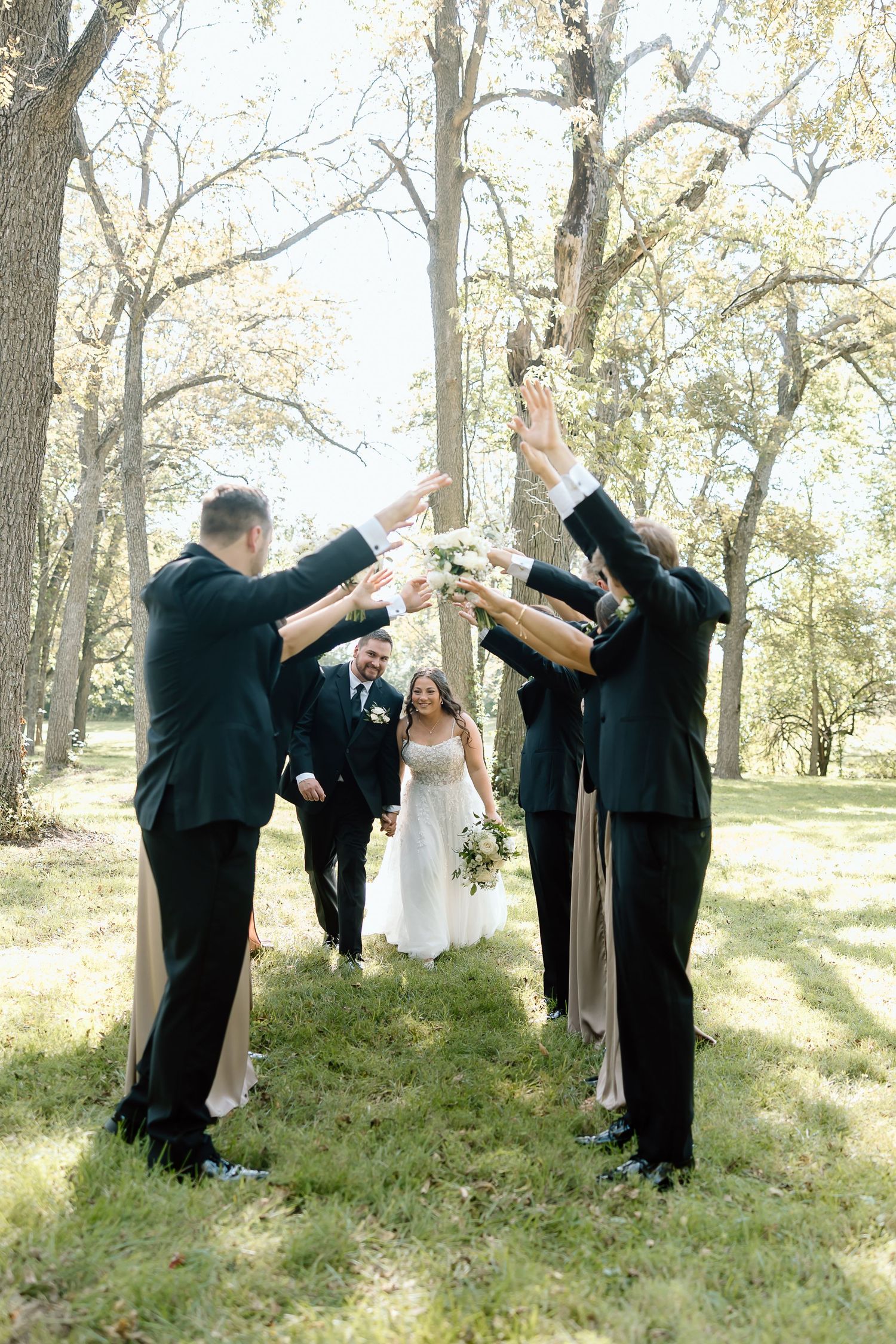 Wedding party in black suits and white dress perform a fun dabbing dance pose sequence in a wooded outdoor setting.