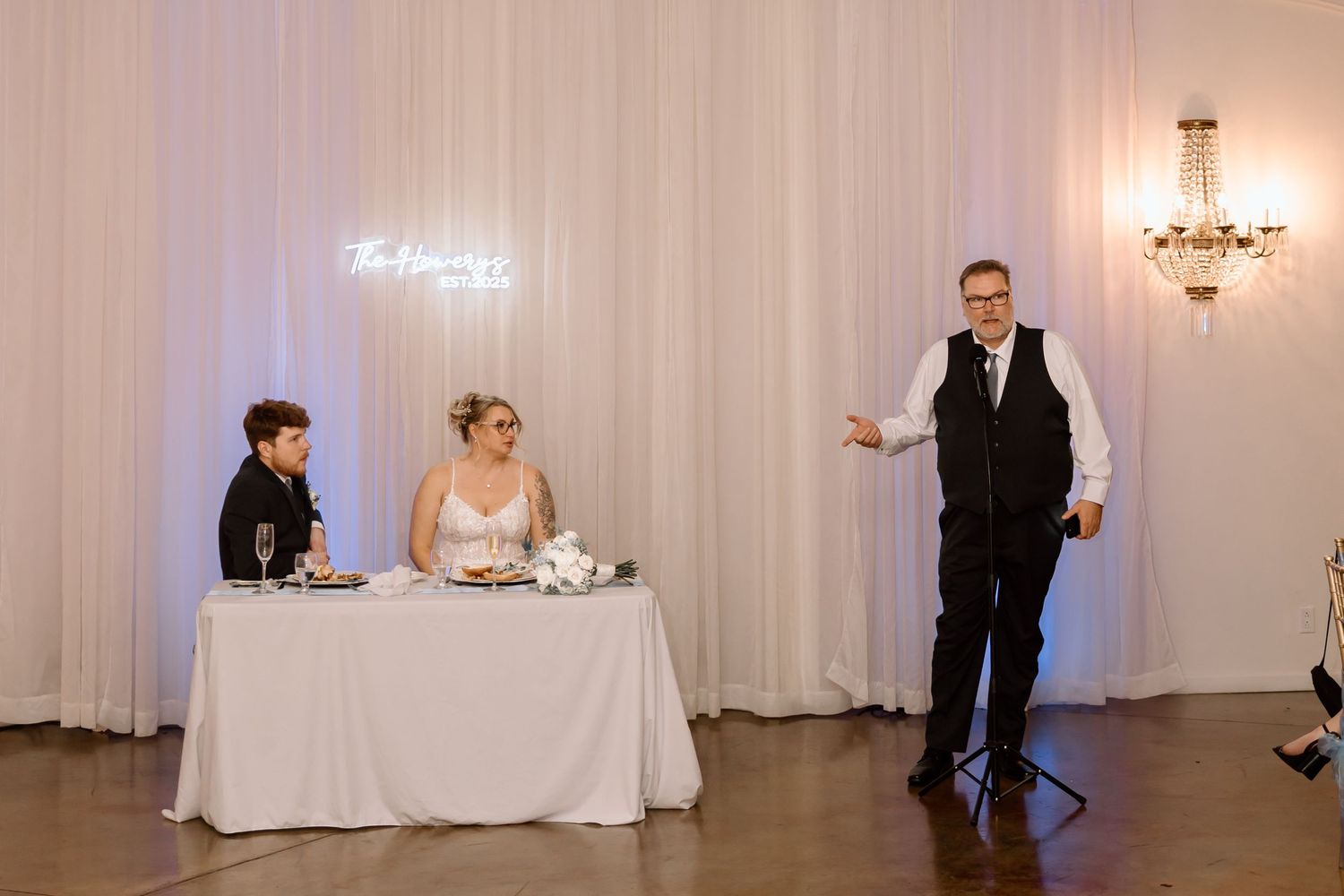 A wedding reception venue with white drapes and elegant chandeliers creates a romantic atmosphere.